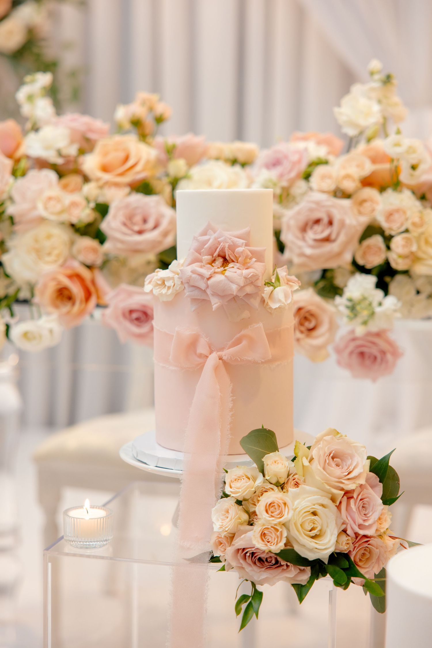 Single-tier white wedding cake adorned with peach and blush roses and a delicate bow ribbon.