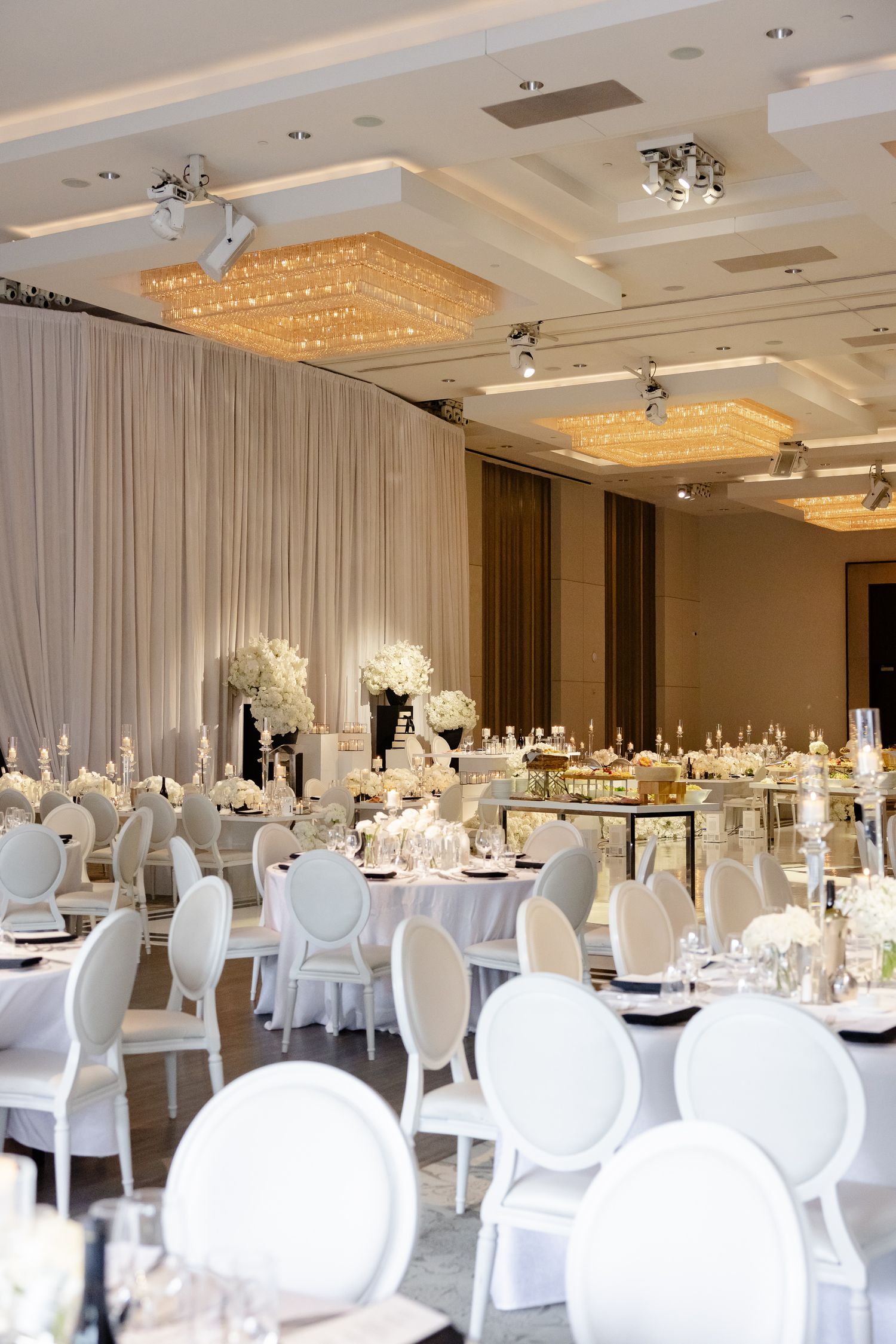 Elegant white ballroom wedding reception with crystal chandeliers, modern oval chairs and luxurious floral centerpieces.