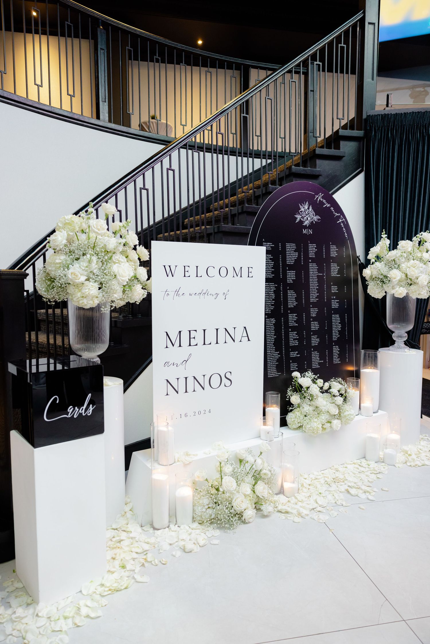 Modern wedding welcome display featuring white hydrangeas, candles and a seating chart against black railings.