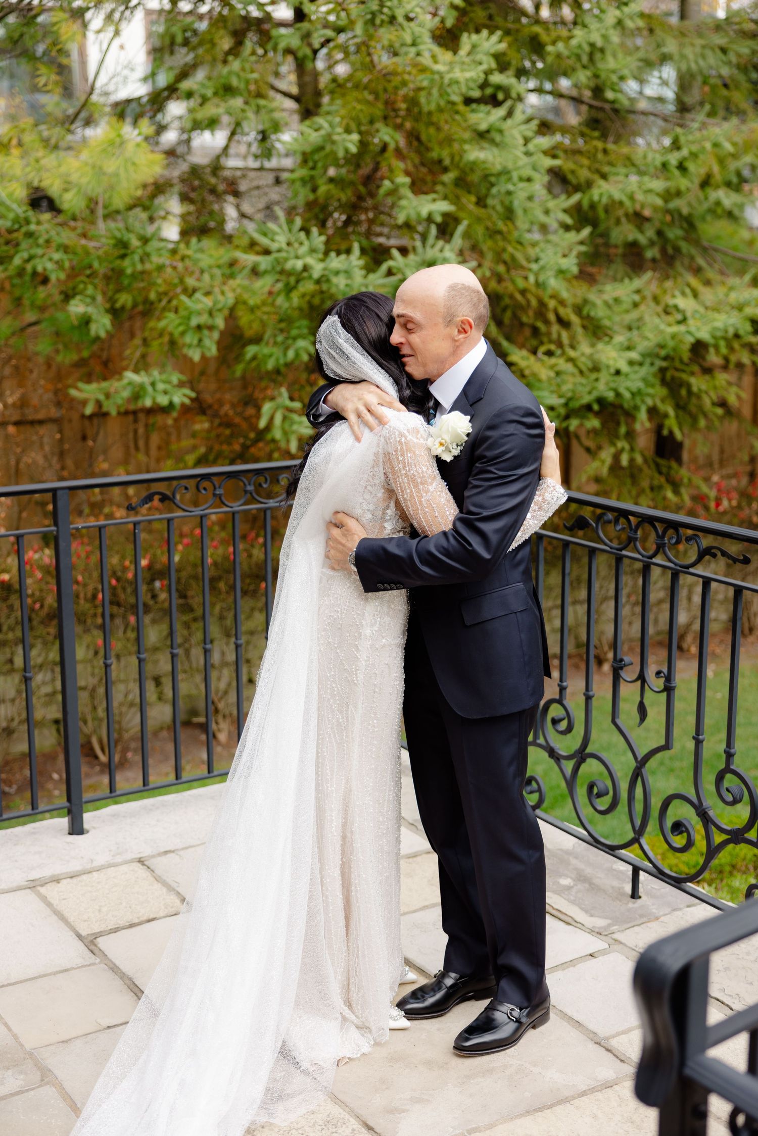 A sweet embrace between newlyweds on an outdoor terrace with lush greenery in the background.