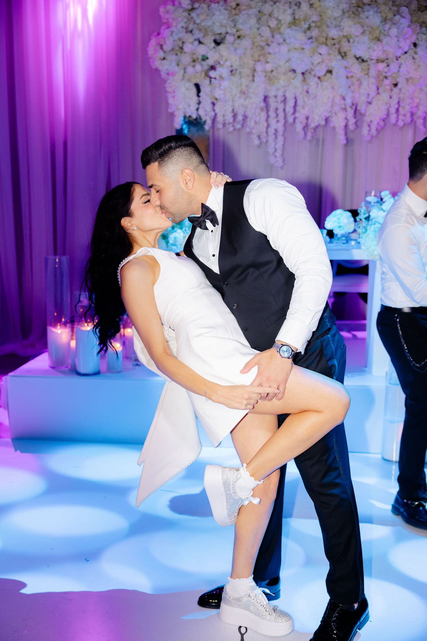 Couple shares intimate dance moment at reception with purple mood lighting and floral decorations.