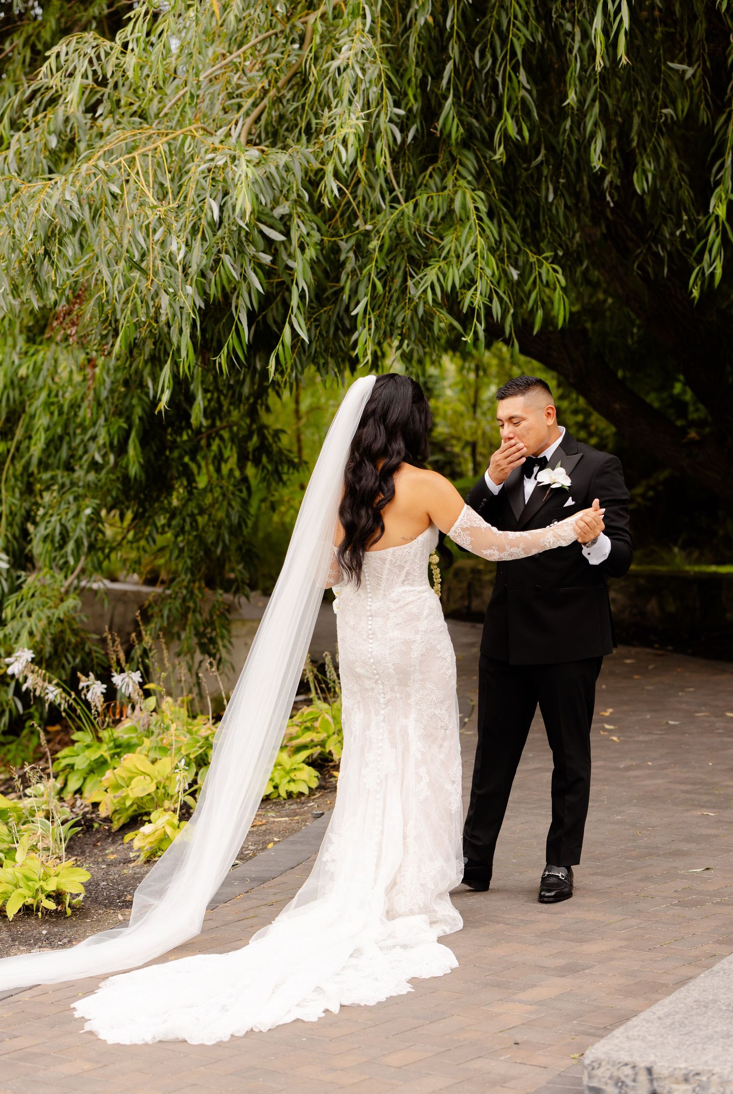 A couple shares their first look moment under a weeping willow tree during an outdoor wedding ceremony.