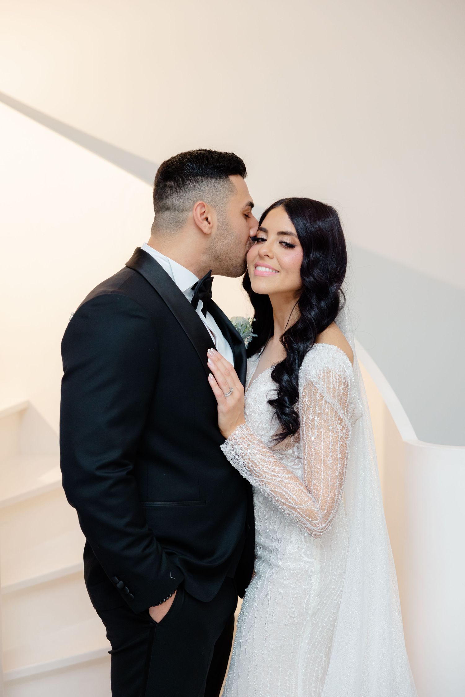 An intimate moment between newlyweds against a white wall, sharing a tender kiss.
