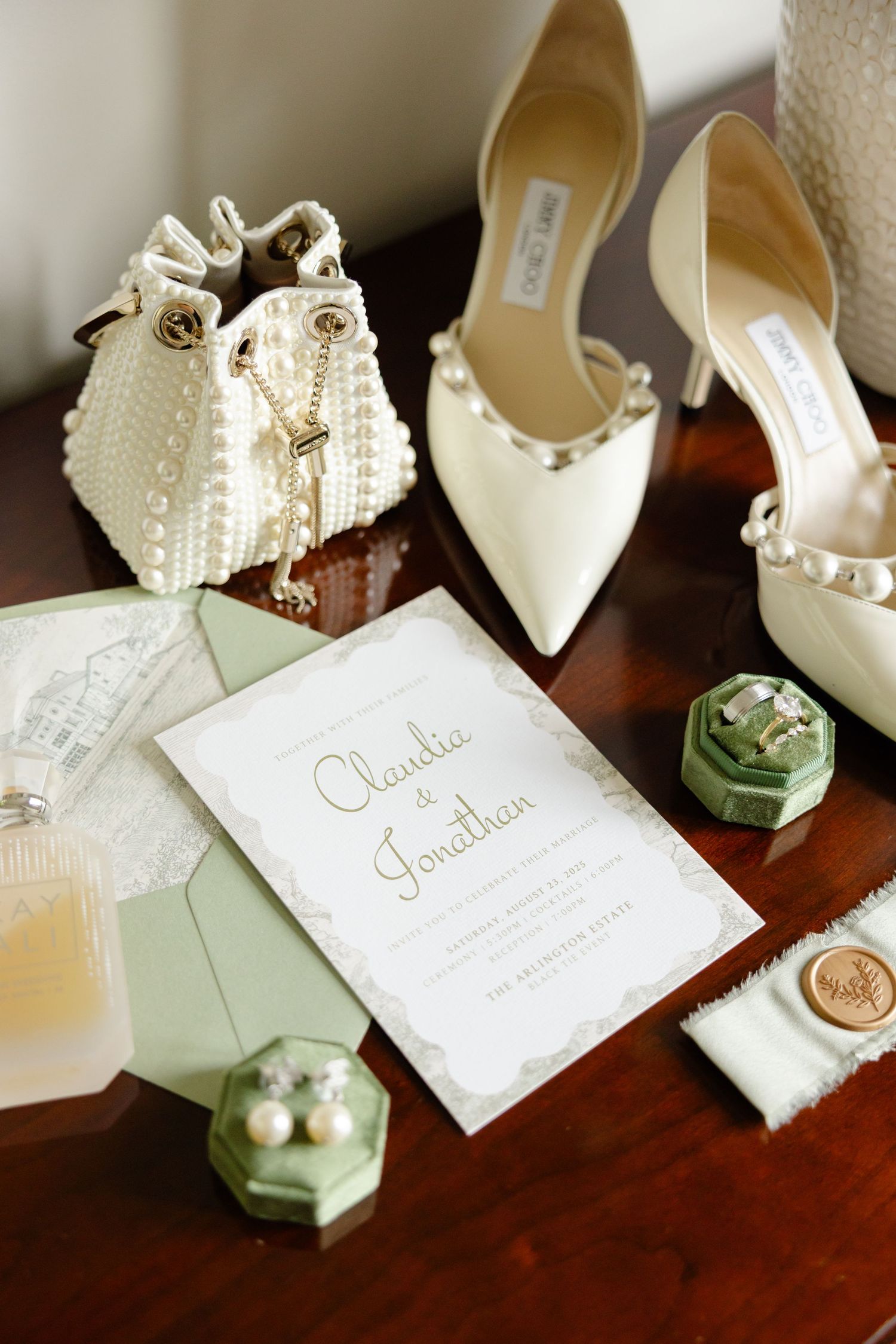 Elegant cream wedding shoes and wedding invitation details arranged artistically on dark wood table surface.