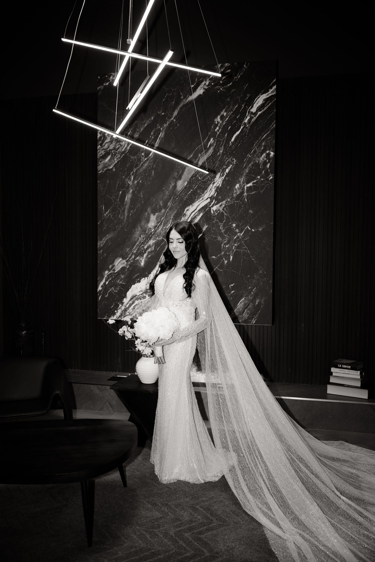 Black and white photo of bride with flowing veil against dramatic marble wall and modern lighting.