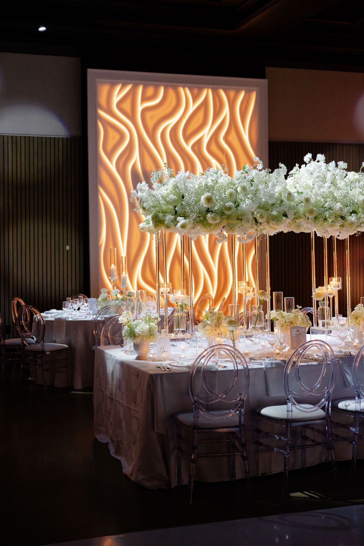 Modern wedding reception table with suspended floral arrangements and illuminated orange backdrop.