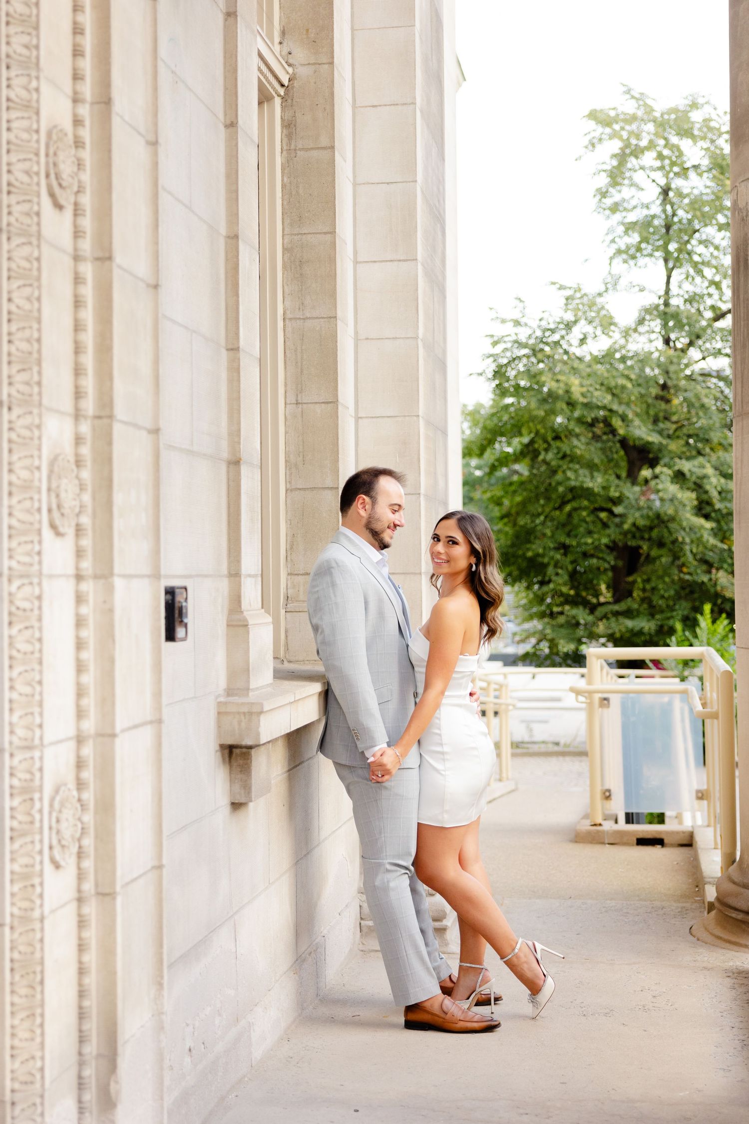 A couple poses together on an elegant columned walkway with greenery in the background.