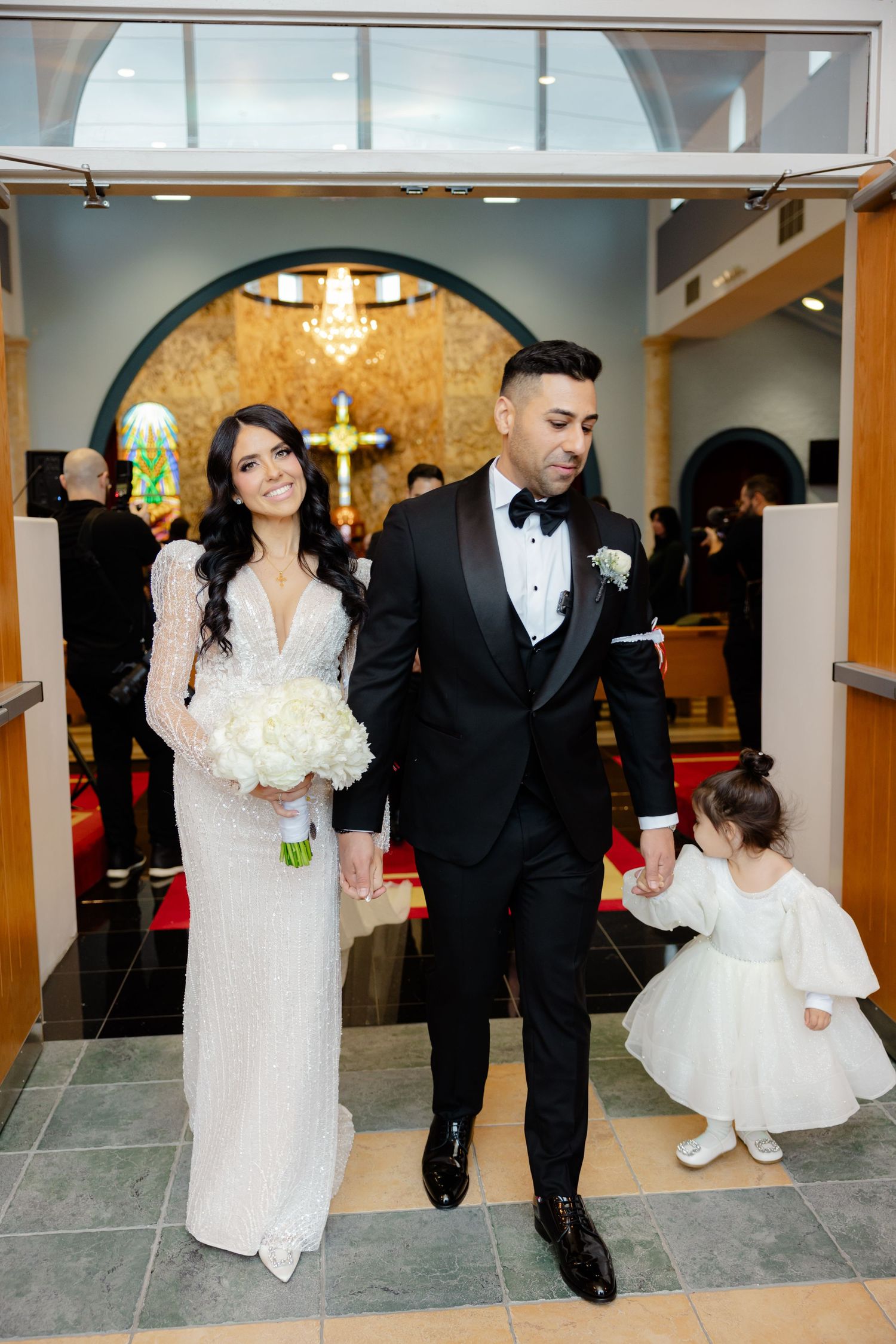 Wedding party exits church beneath modern arched doorway with tiled floor.