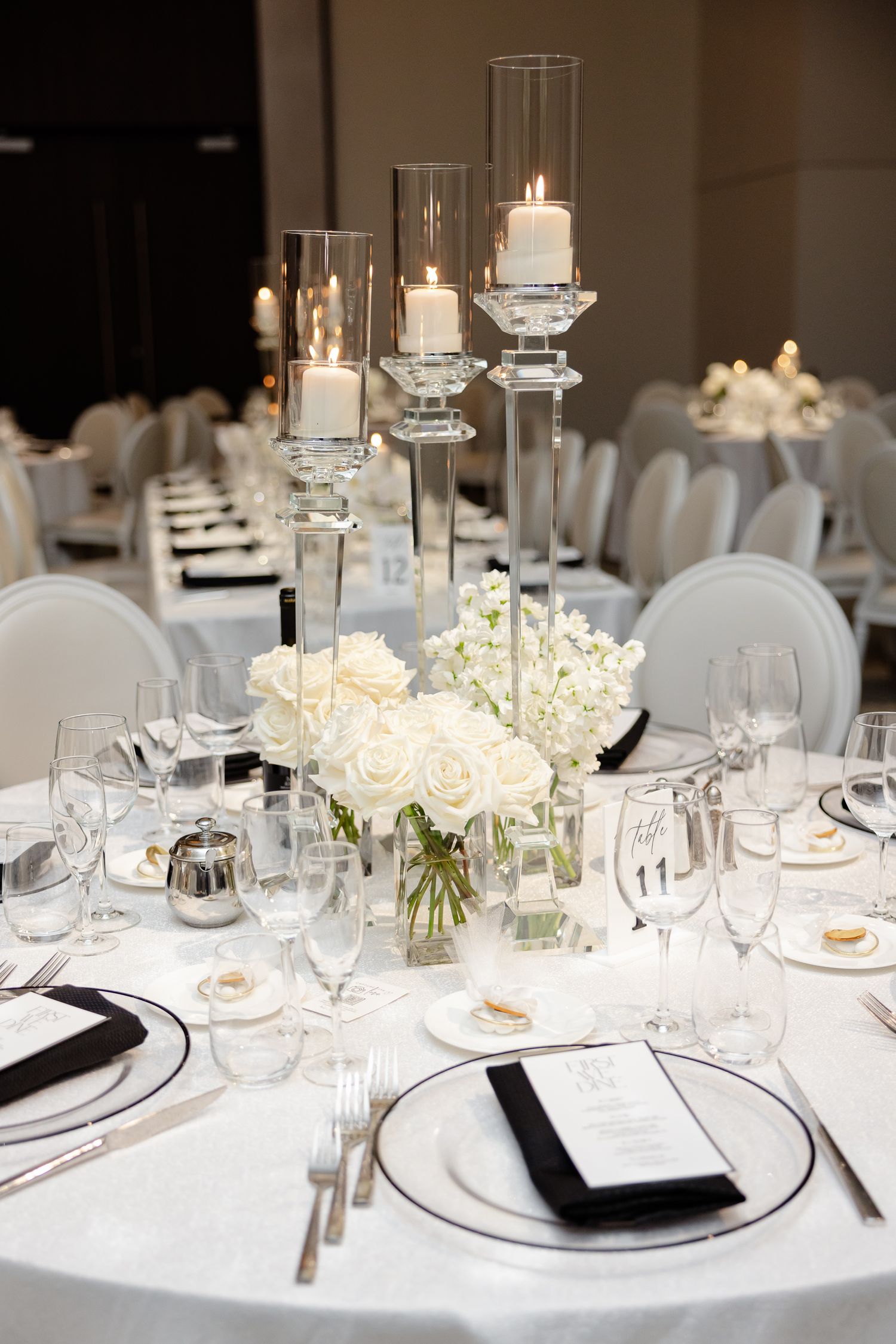 Elegant white wedding reception table settings with crystal candleholders, white roses and pristine place settings.