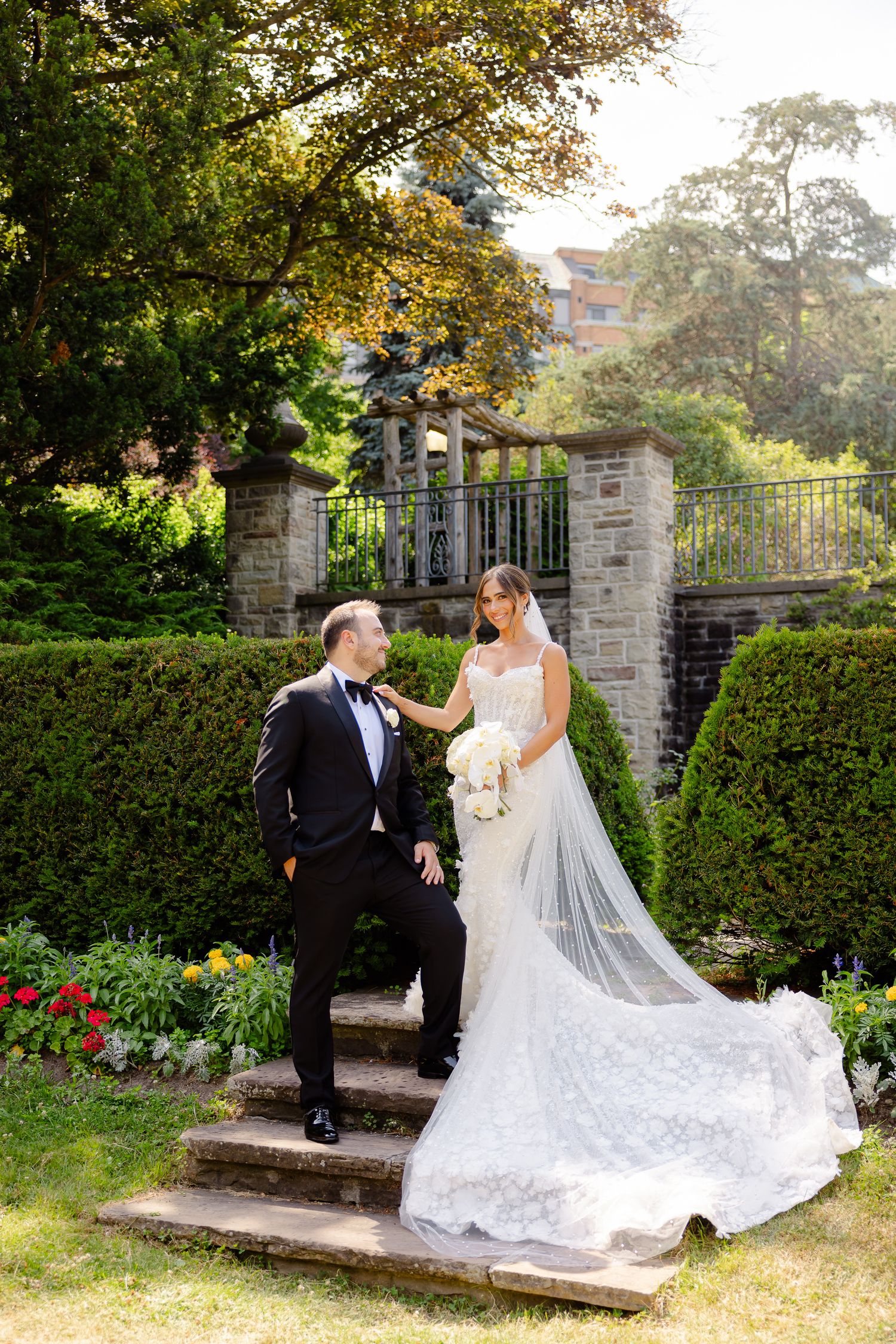 A couple on stone garden steps surrounded by lush greenery and manicured hedges on their wedding day.
