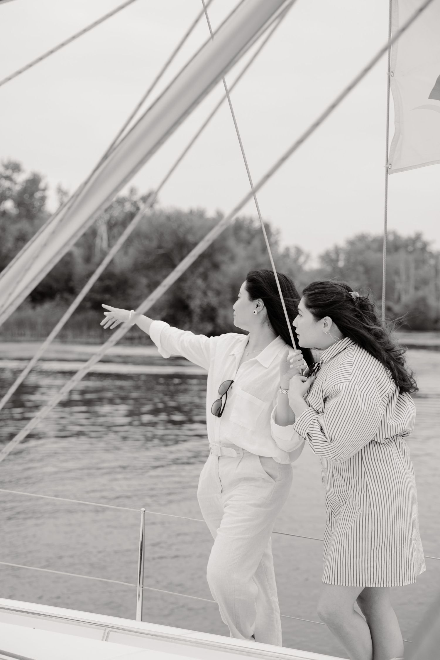 Two people enjoying a sailing trip together on a boat, pointing towards the horizon in black and white.