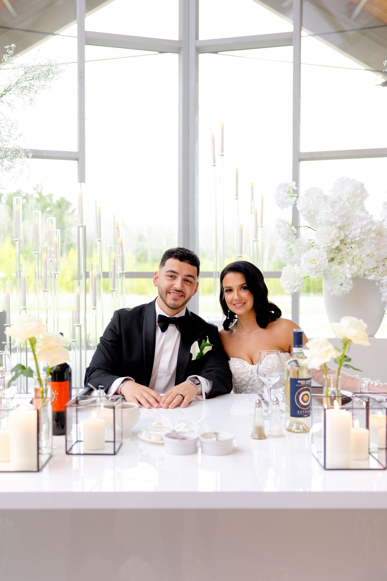 Elegant wedding couple seated at their sweetheart table with white floral decorations and modern table settings.
