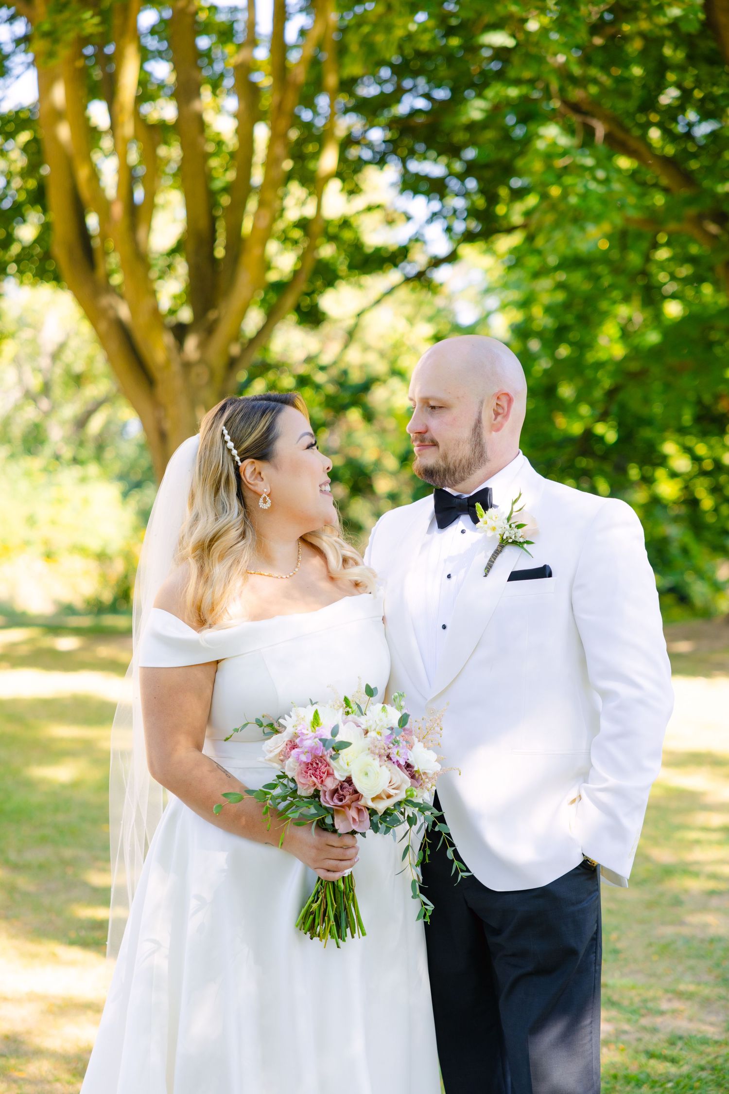 Romantic wedding moment captured as couple shares loving gaze under sunlit trees.