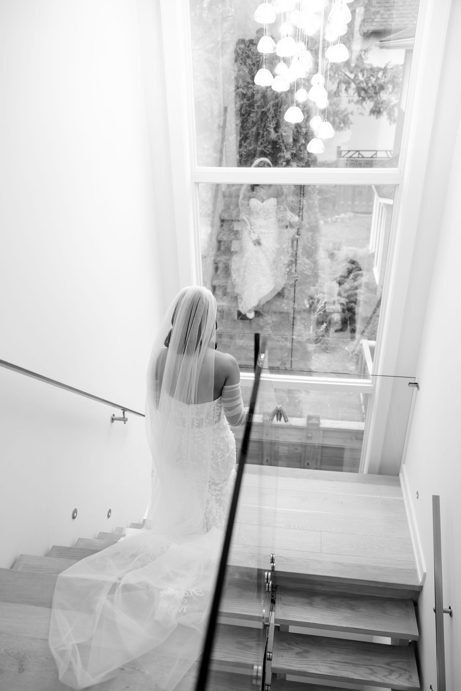 A bride in a flowing white dress descends a modern staircase in black and white photography.