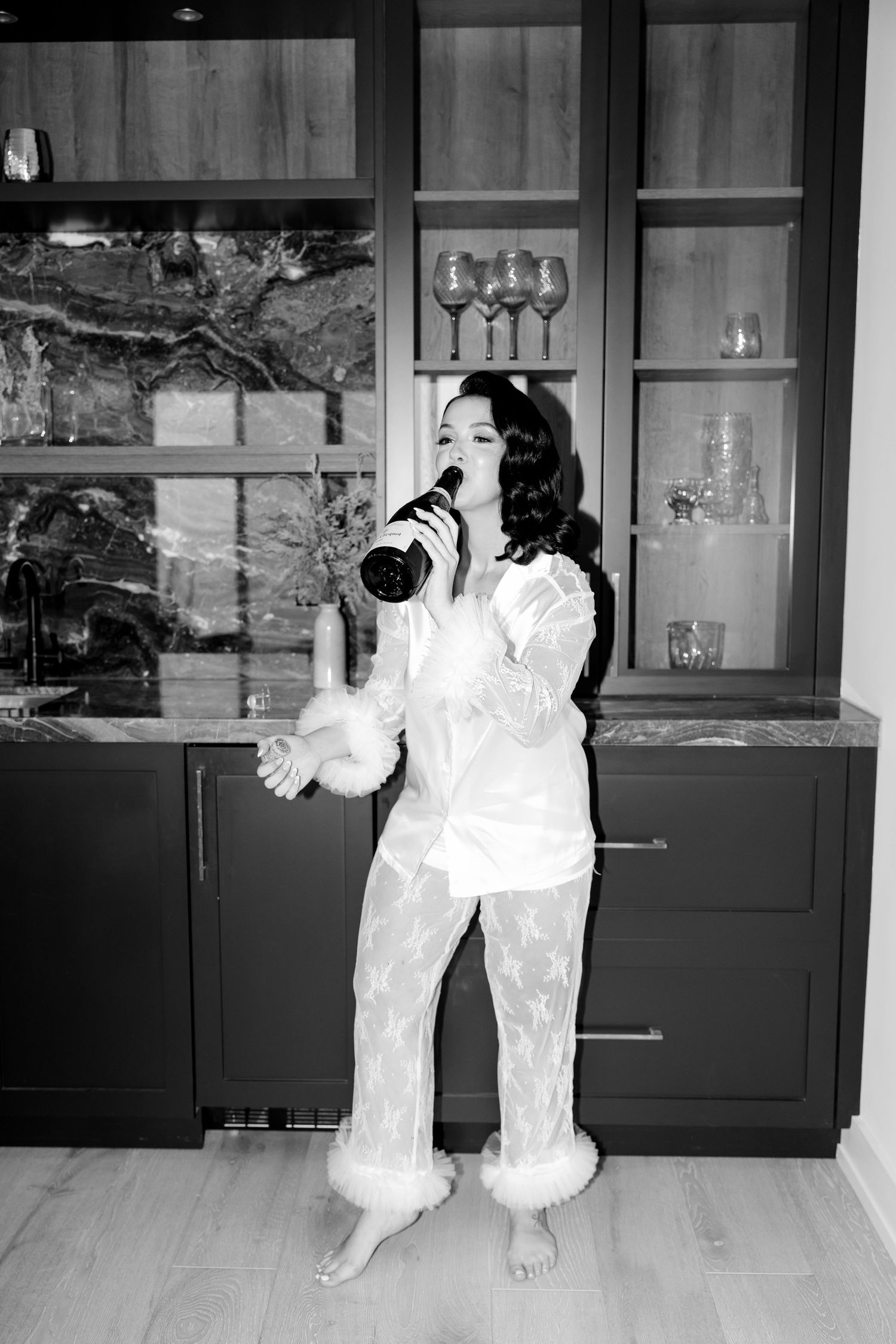 Black and white photo of woman in white outfit drinking from champagne bottle.