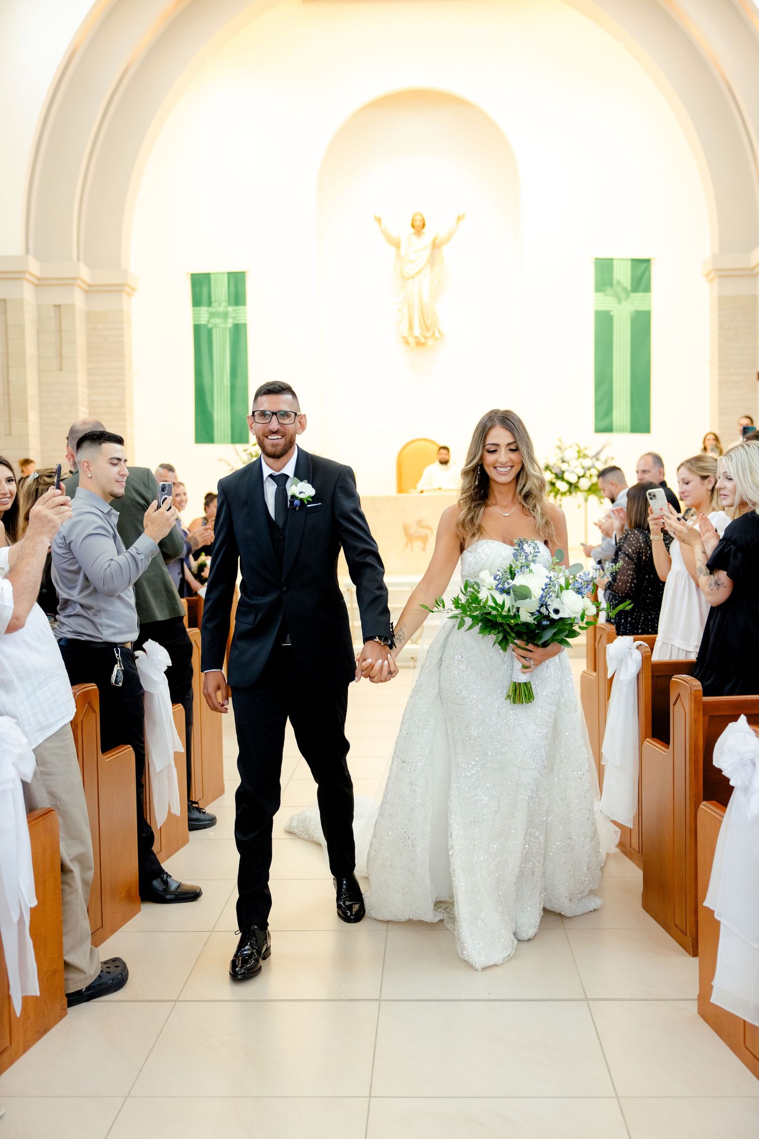 Bride and groom exit church ceremony while guests celebrate in the pews.