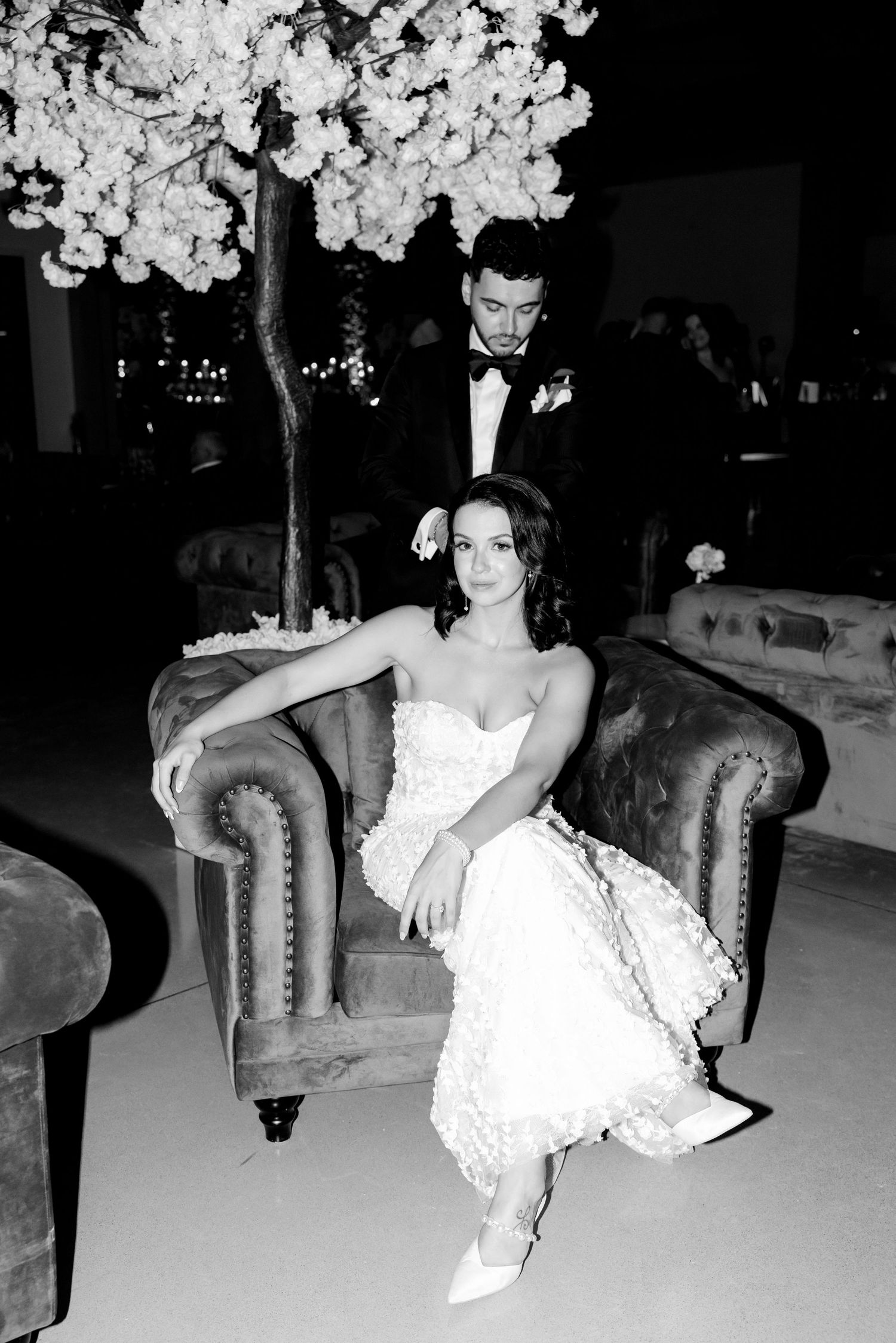 Black and white portrait of couple on vintage sofa under decorative cherry blossom tree.