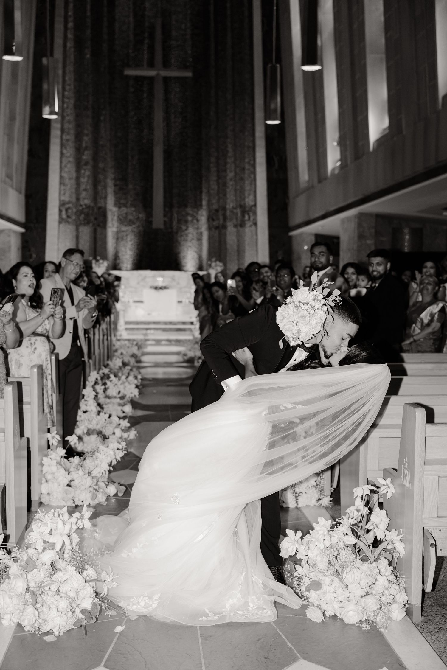 A black and white image of a romantic wedding dip kiss in a church setting.