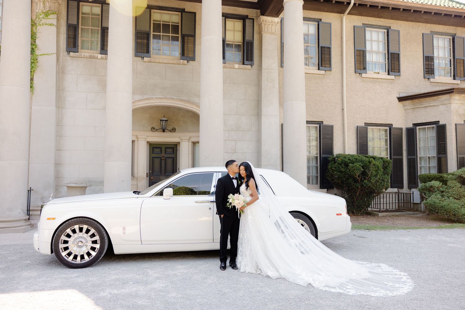 Wedding photography featuring a couple and white luxury vehicle against Mediterranean-style architecture.