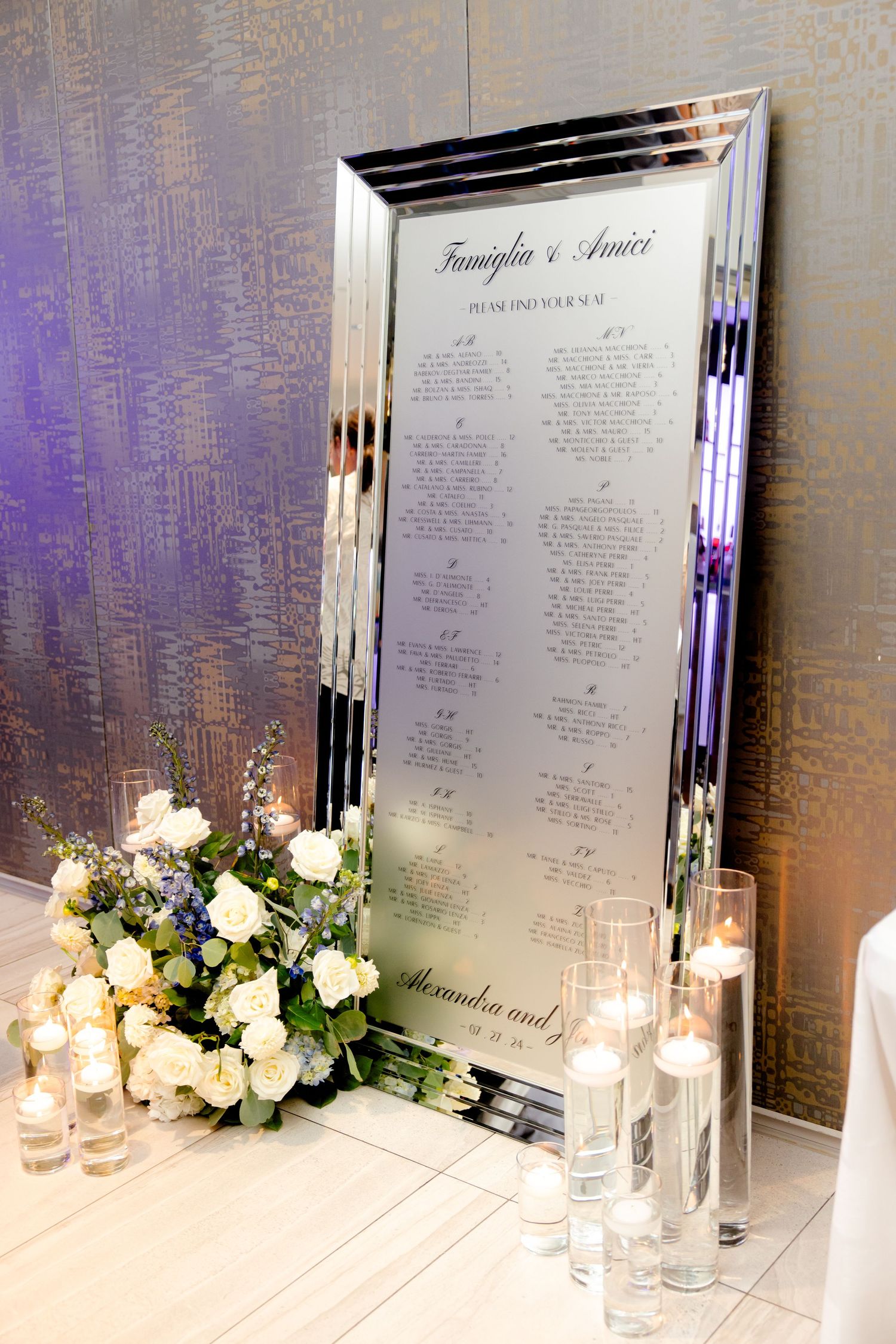 Elegant mirrored frame displaying wedding seating chart with floral accents and candles.