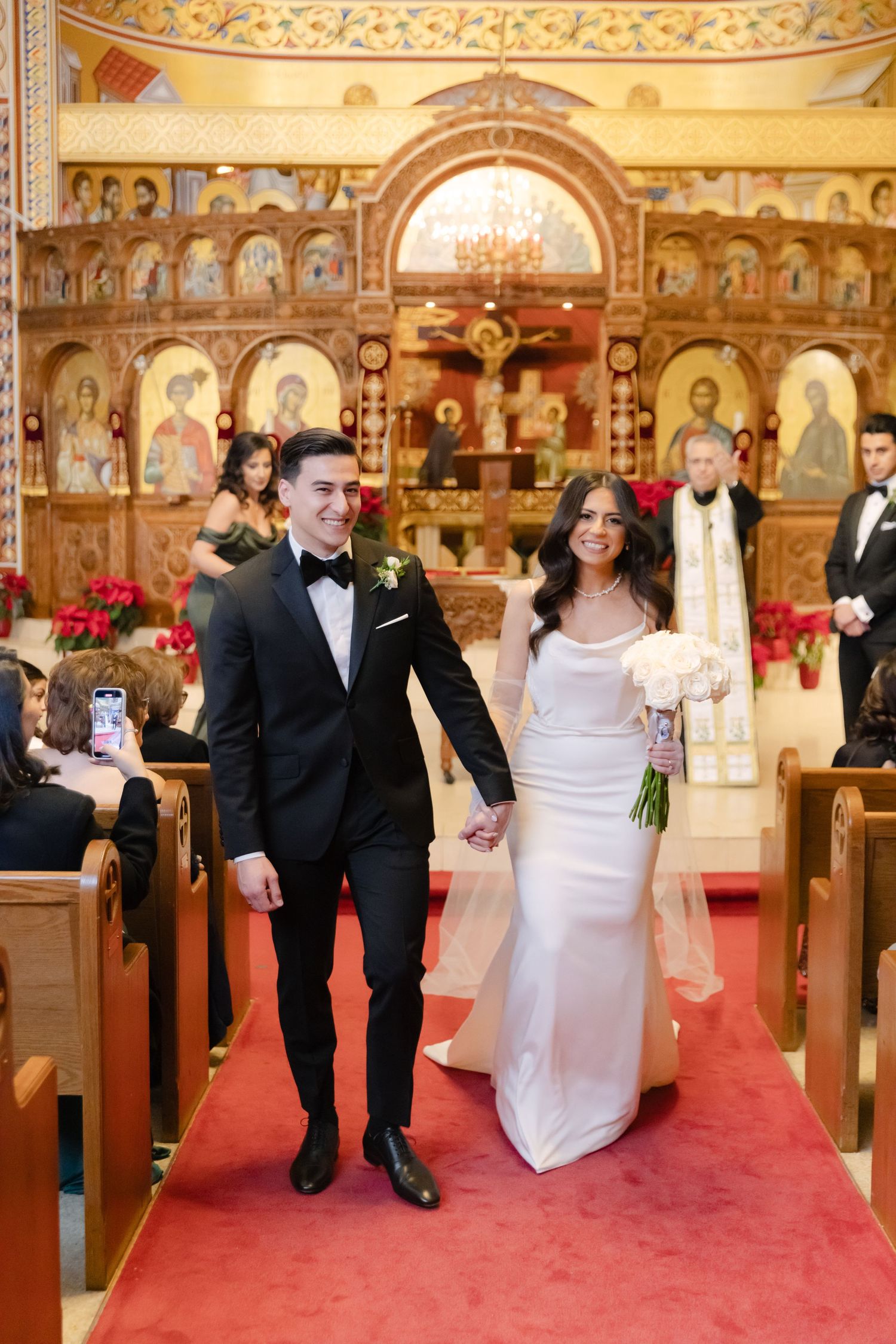 Happy couple walks down church aisle after wedding ceremony with guests watching.