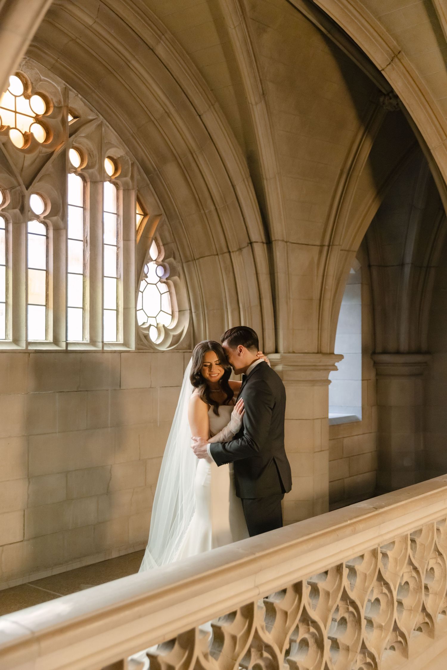 A wedding couple shares a tender moment beneath ornate gothic windows and vaulted stone arches.