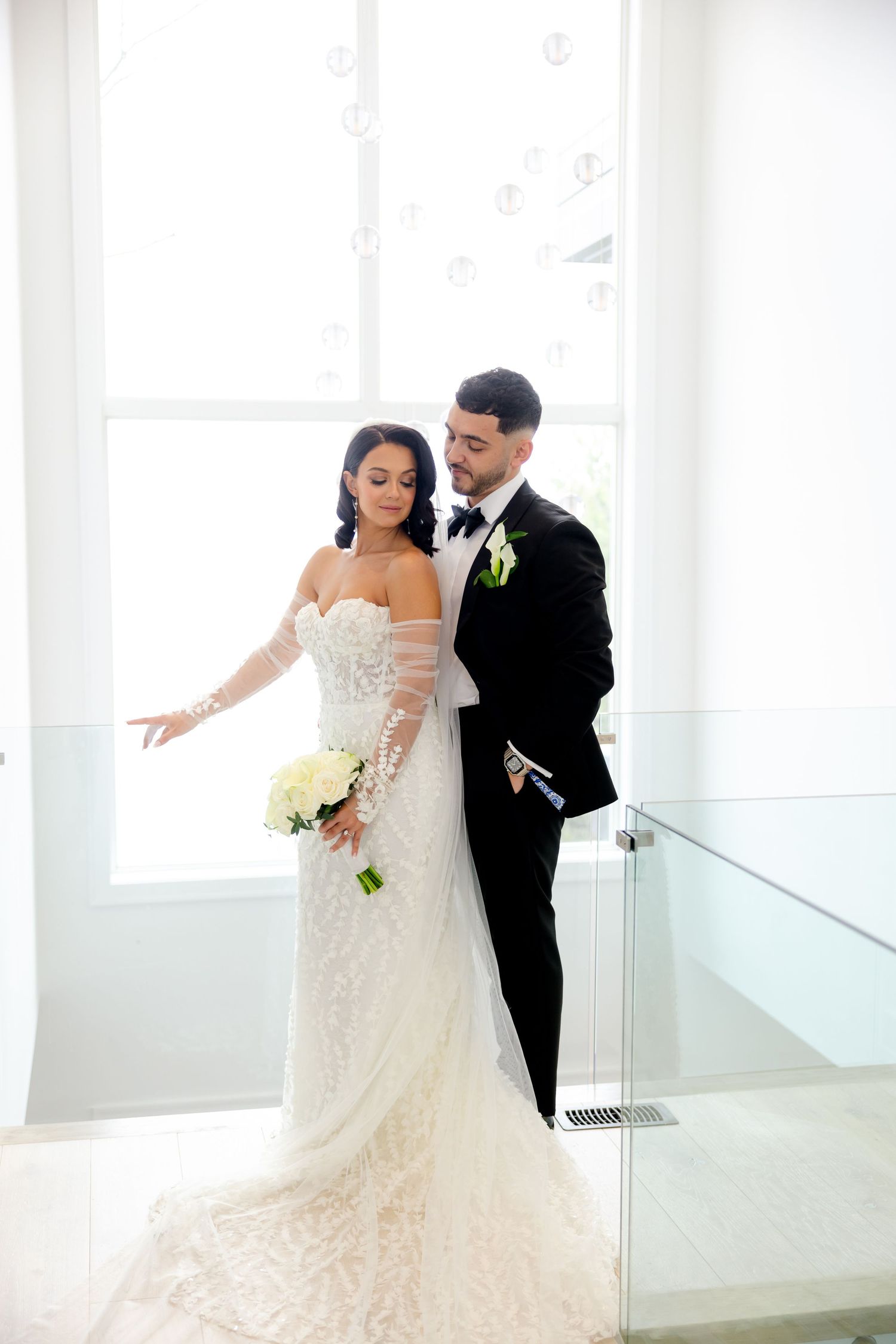 Wedding couple embraces near bright window in modern white interior.