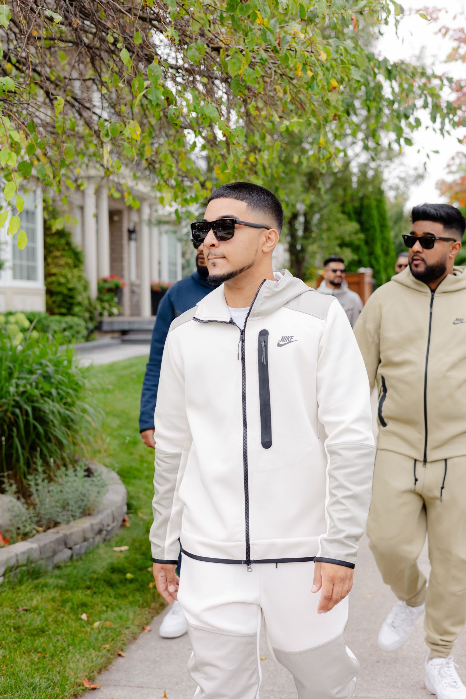 A group in casual athletic wear poses in front of landscaping and a residential building.