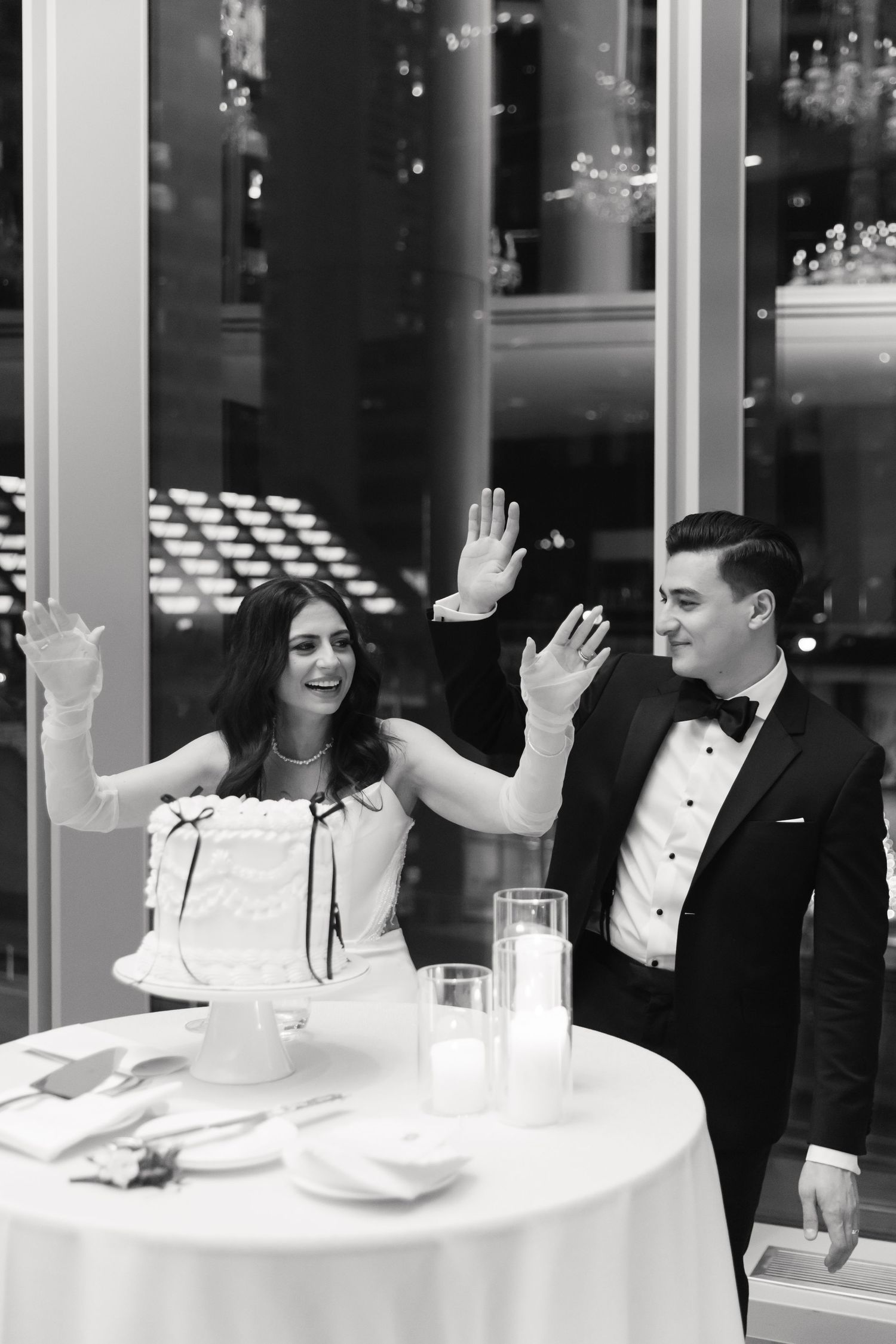 A couple in formal attire raises their hands joyfully during a wedding celebration.
