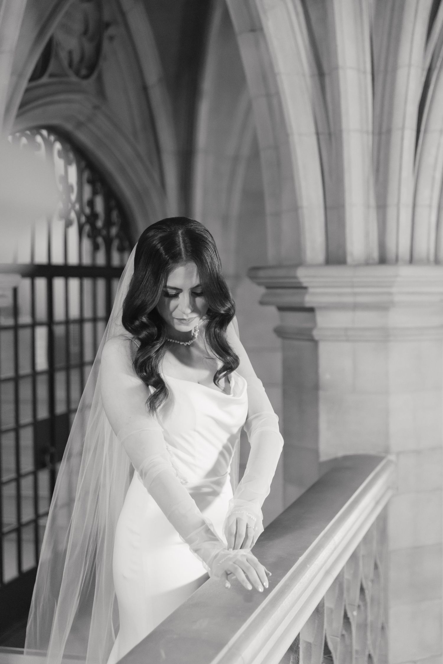 Bride in flowing veil poses elegantly on historic stone balcony.