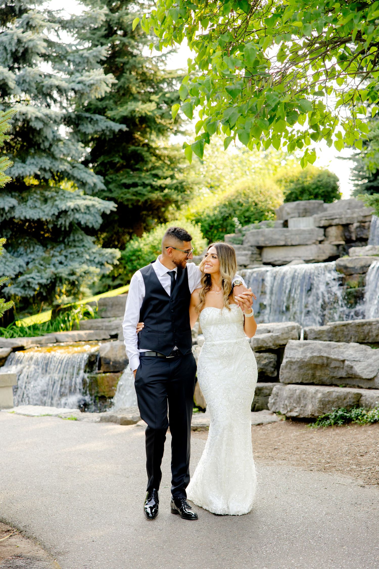 Candid wedding moment captured near garden waterfall with lush greenery.