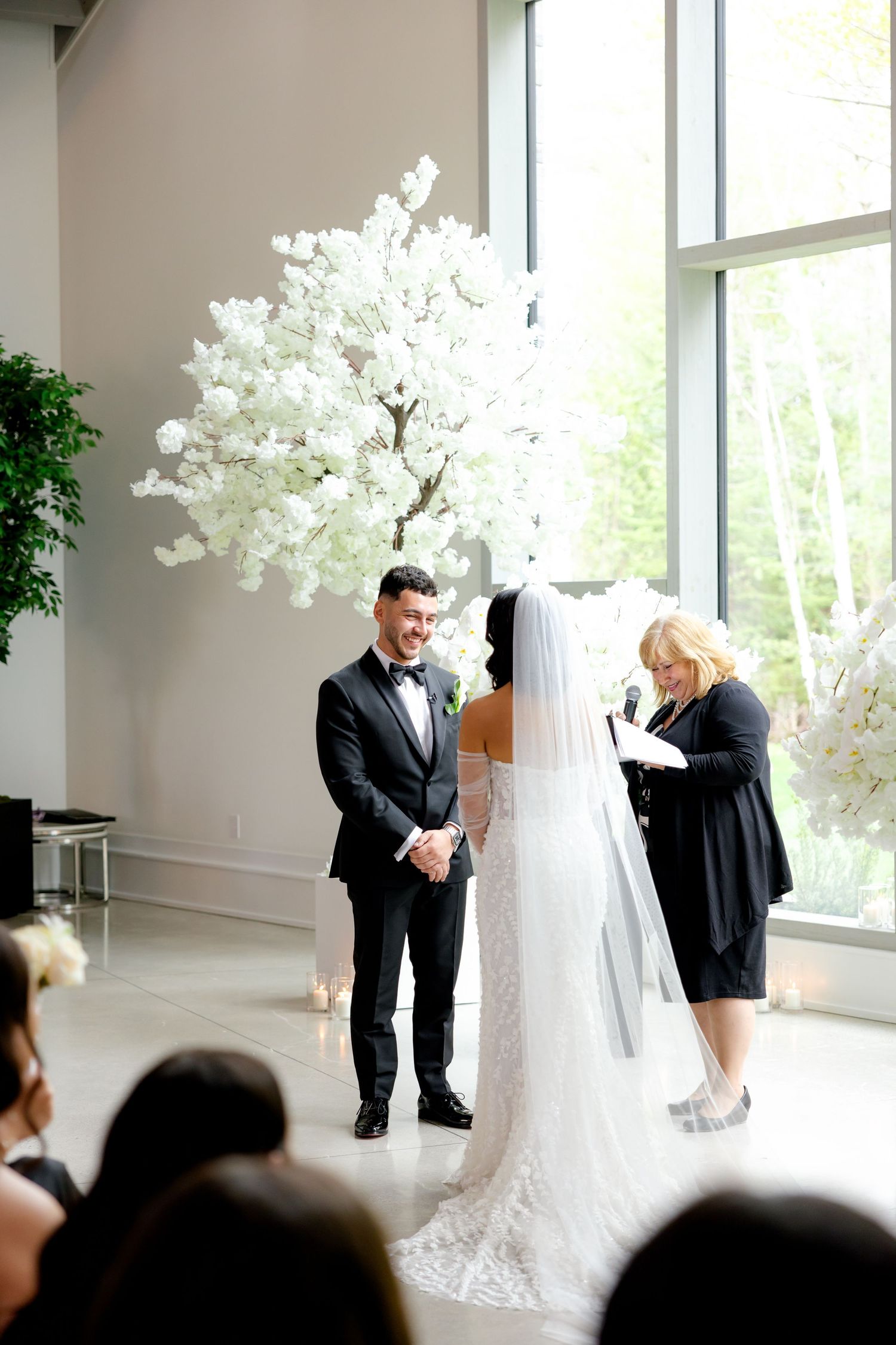 An intimate wedding ceremony with a stunning white floral tree display and natural window lighting.