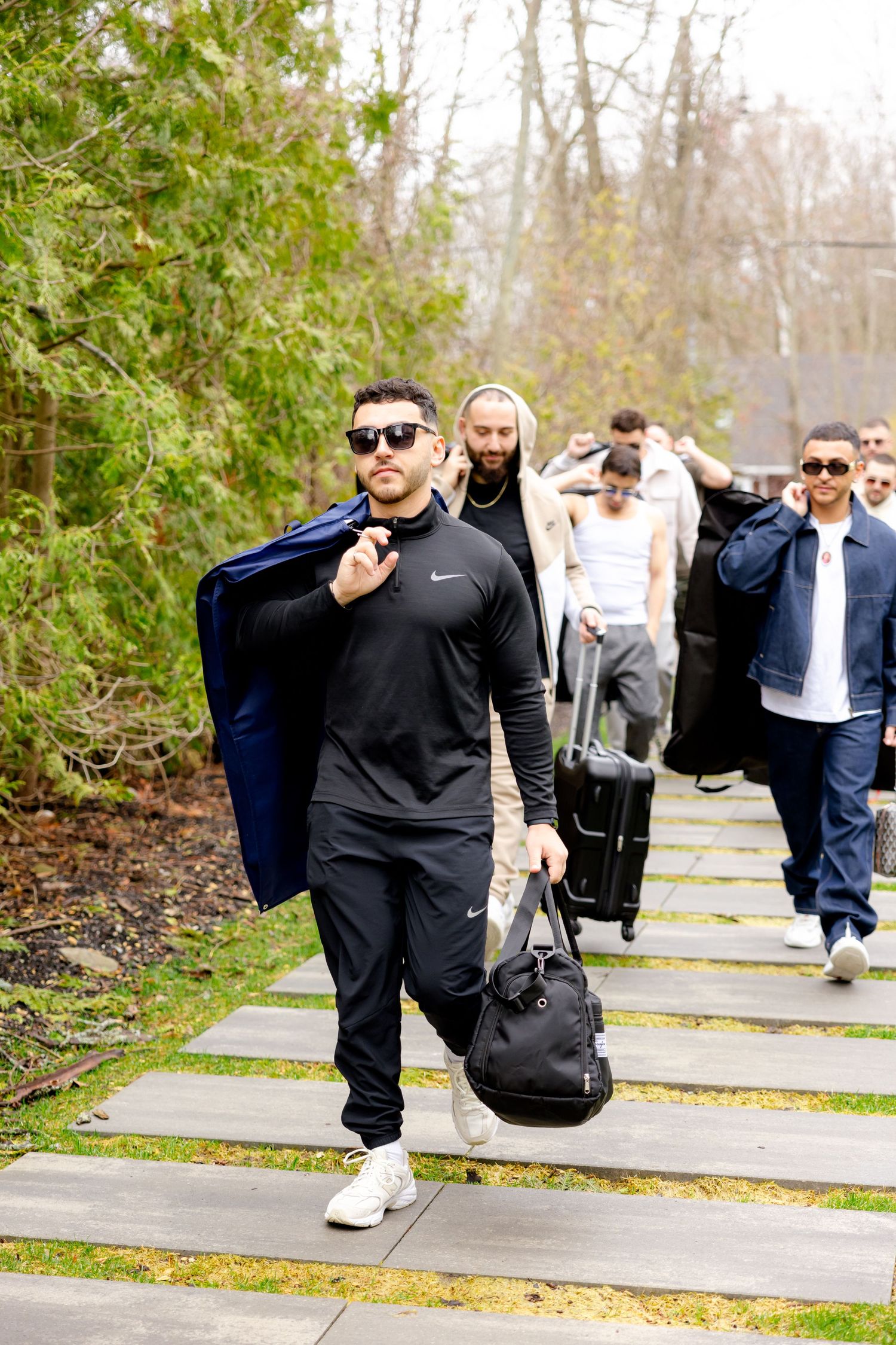 Group walking along outdoor pathway carrying bags and coats on spring day.