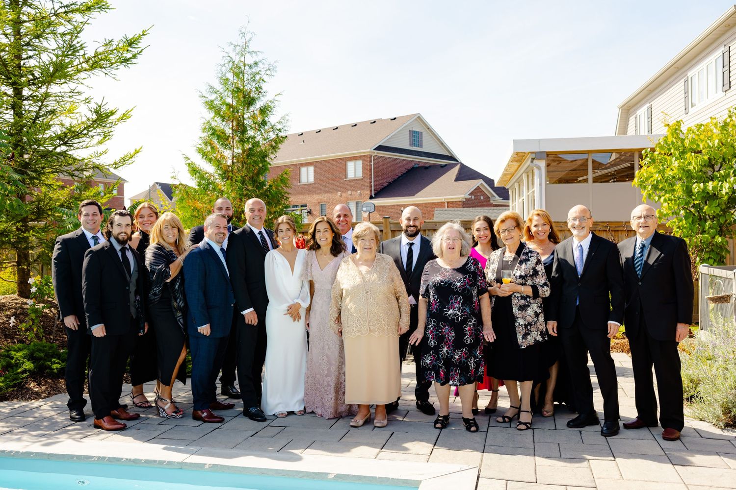 Large wedding party group photo taken outdoors by a pool on a sunny day.