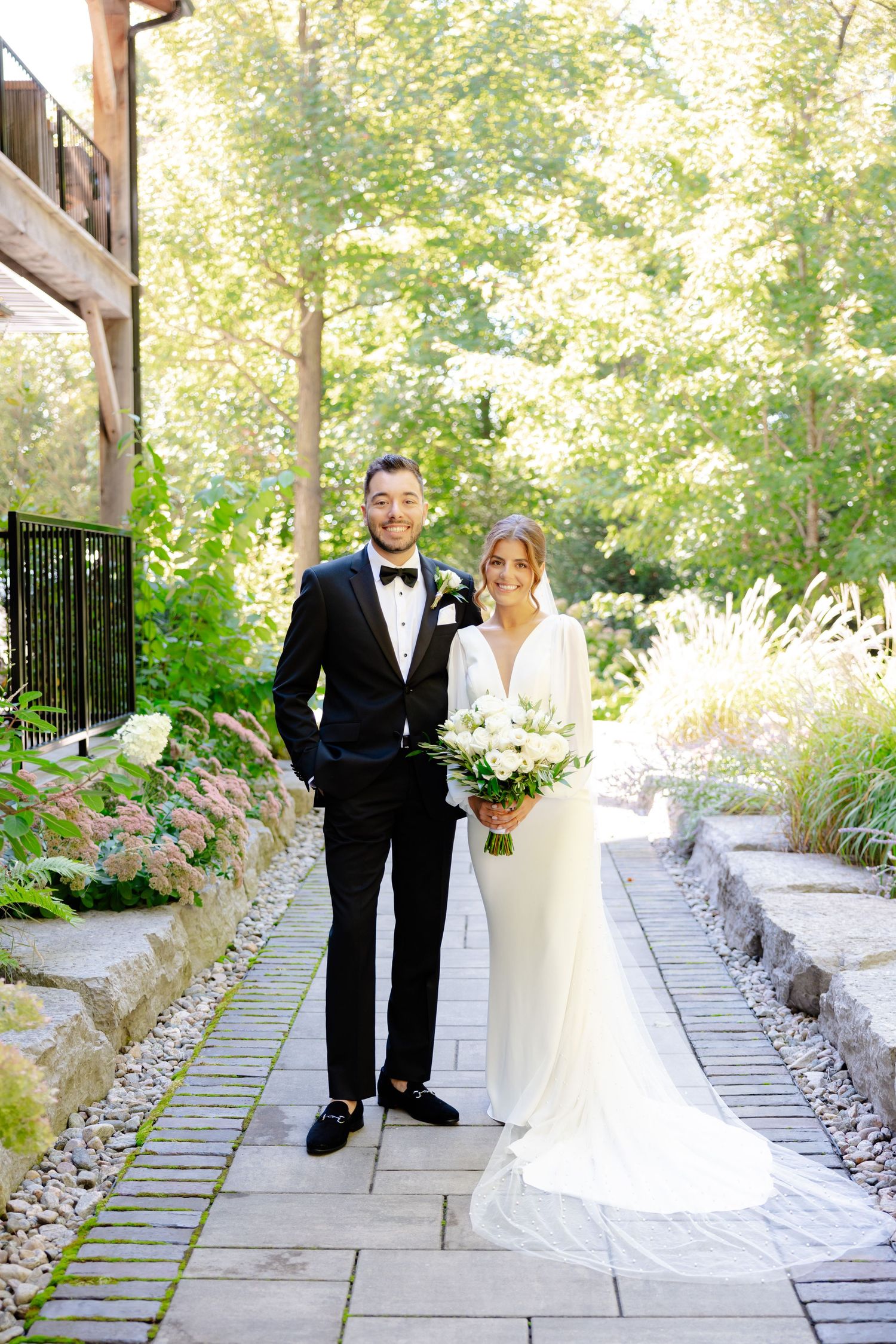 Couple poses for formal wedding portrait on stone path with verdant garden surroundings.