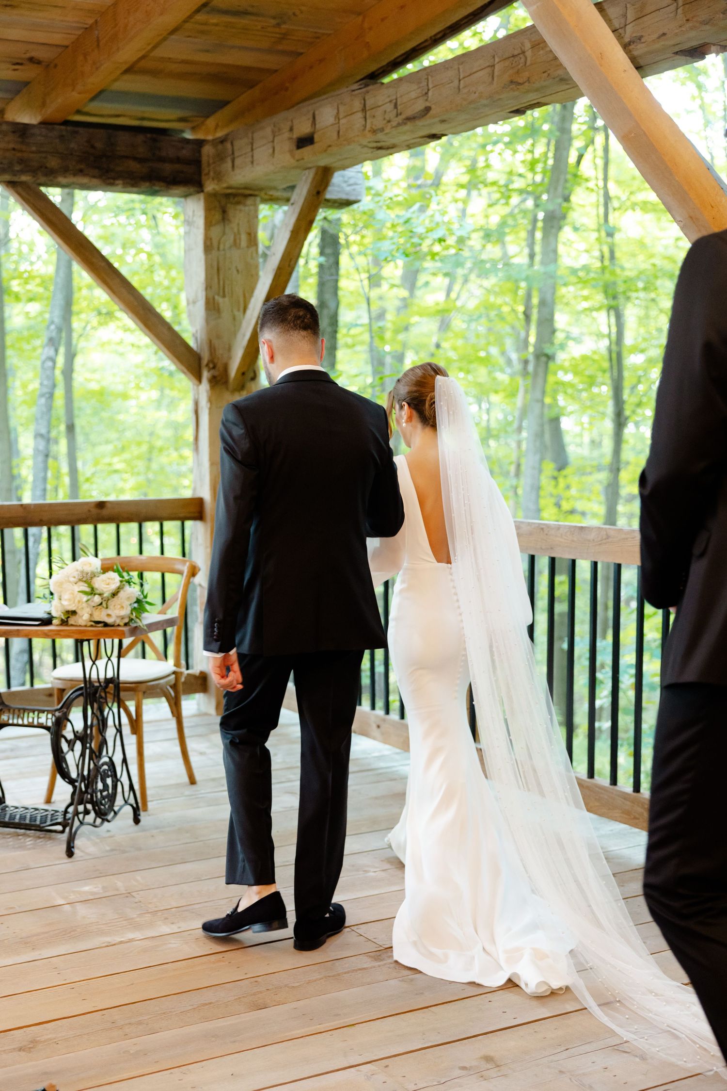 Wedding ceremony in wooden pavilion with antique sewing table and forest views.
