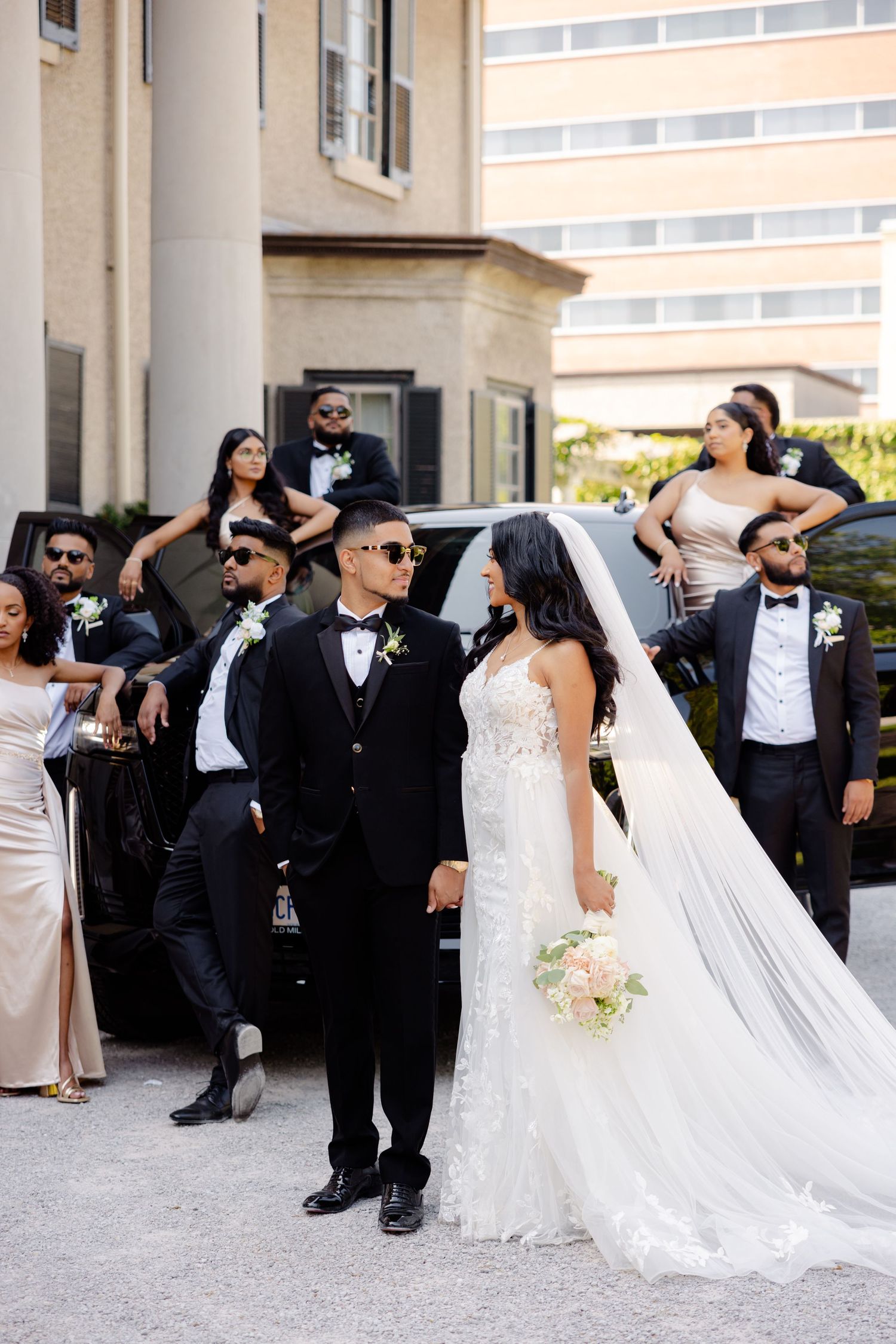 A wedding party celebrates with joyful expressions outside an elegant venue with columns.