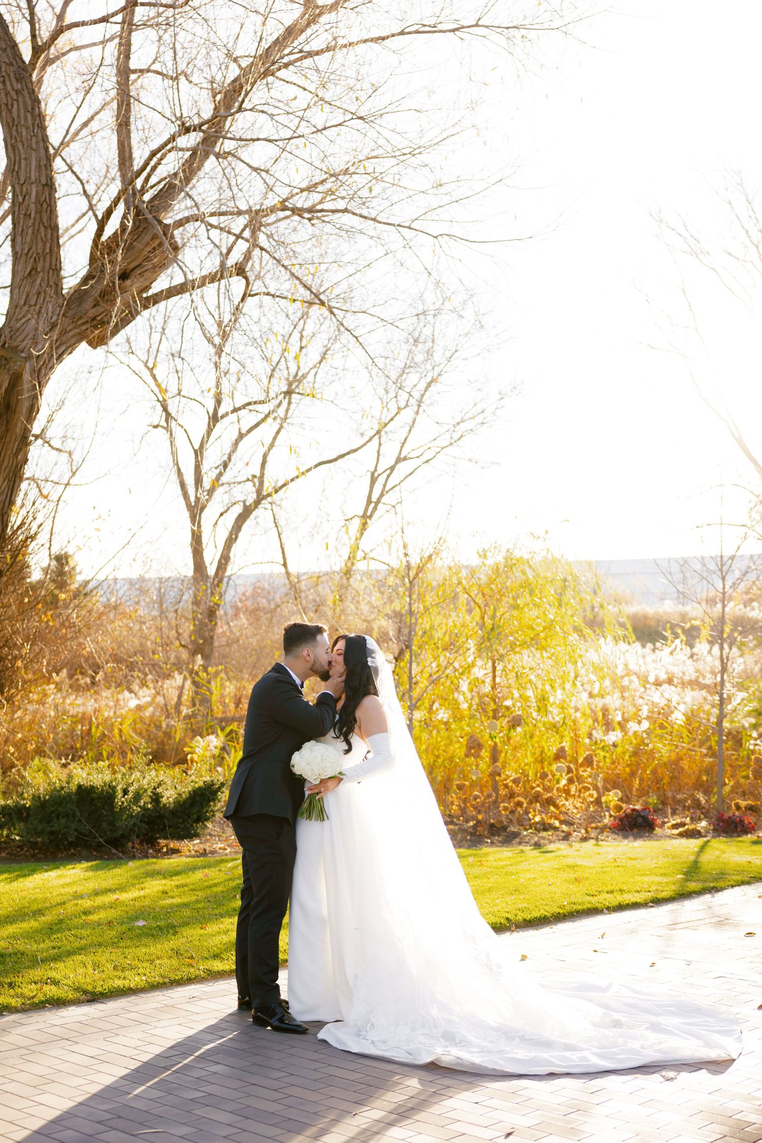 Romantic wedding photo with couple sharing tender moment amid fall foliage and sunlight.