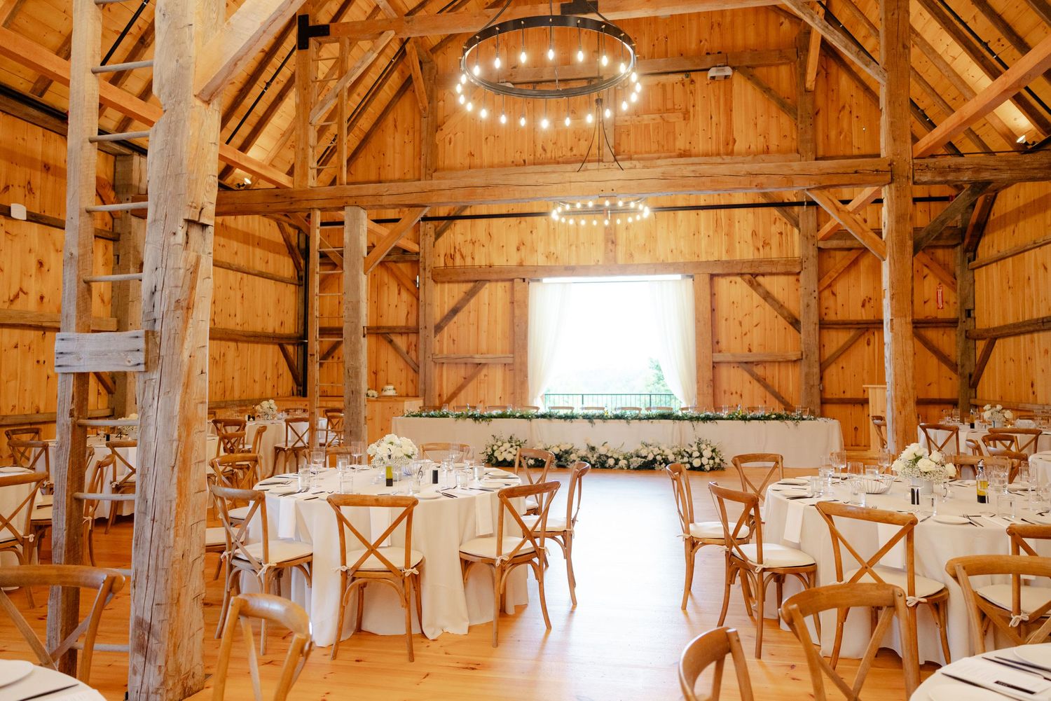Rustic barn wedding reception venue with wooden beams and hanging chandeliers.