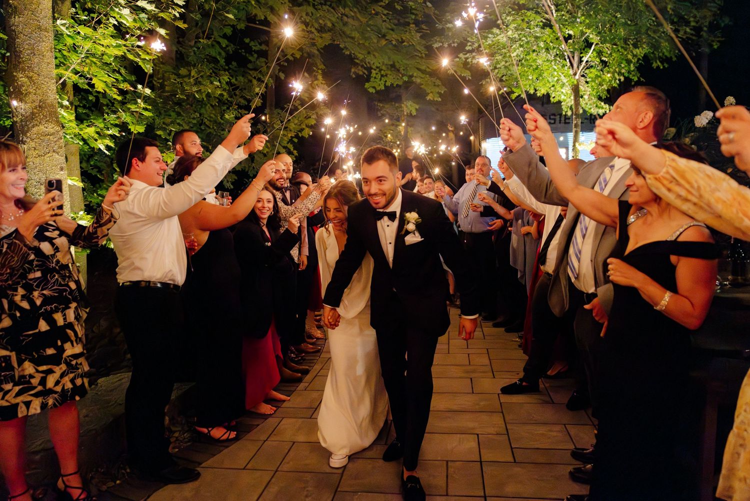 Guests line a garden path holding sparklers as newlyweds walk through.