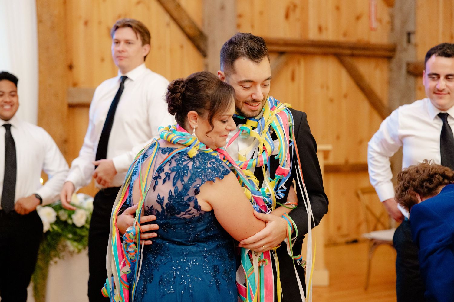 A joyful dance moment at a barn wedding with colorful streamers and wooden beam details.
