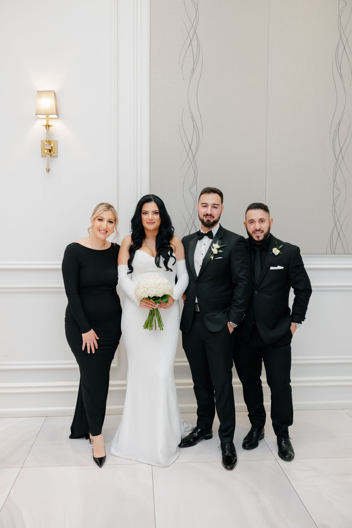 Formal wedding group photo with bride in white gown surrounded by guests in black attire.