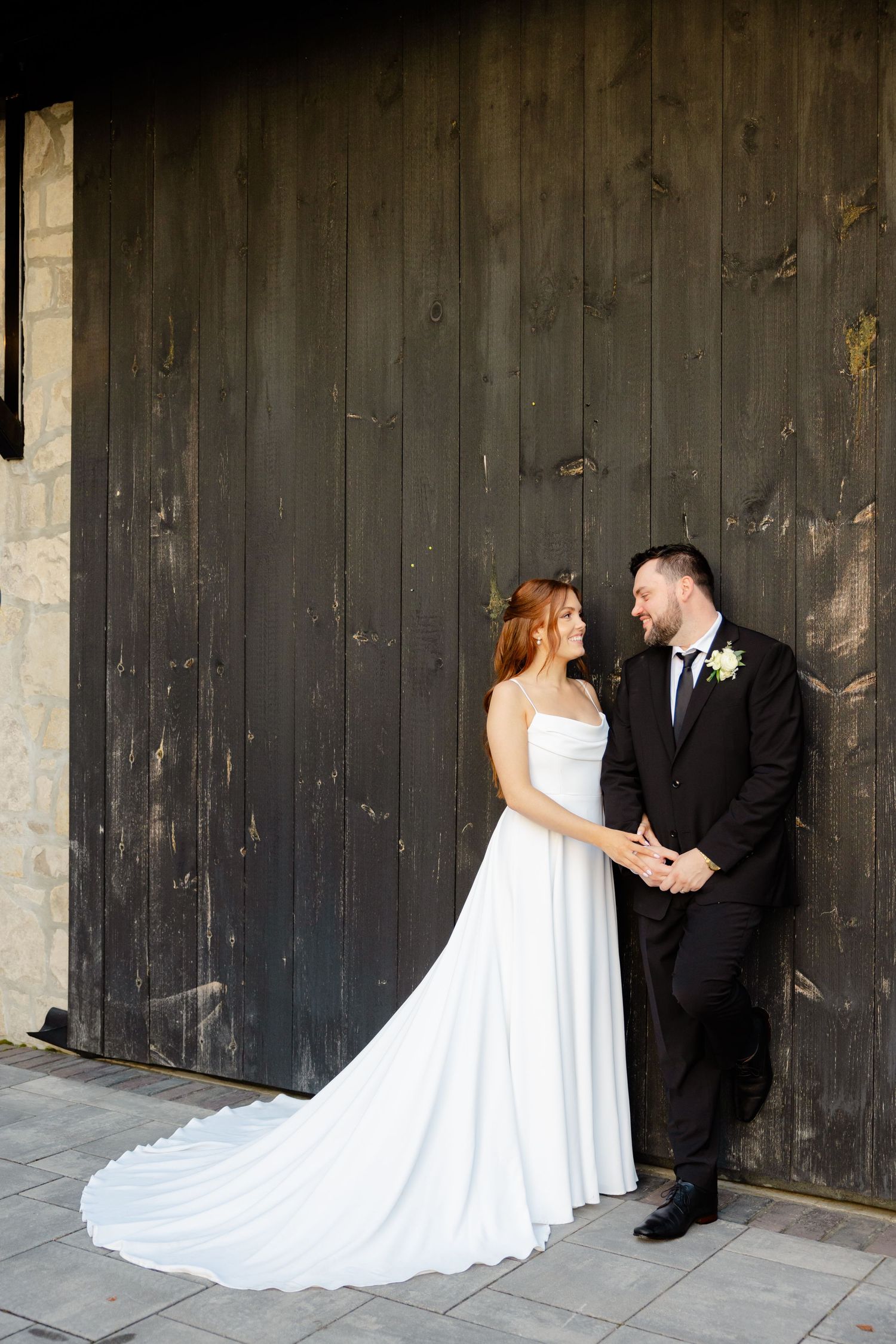 Couple shares intimate moment against rustic wooden backdrop in wedding attire.