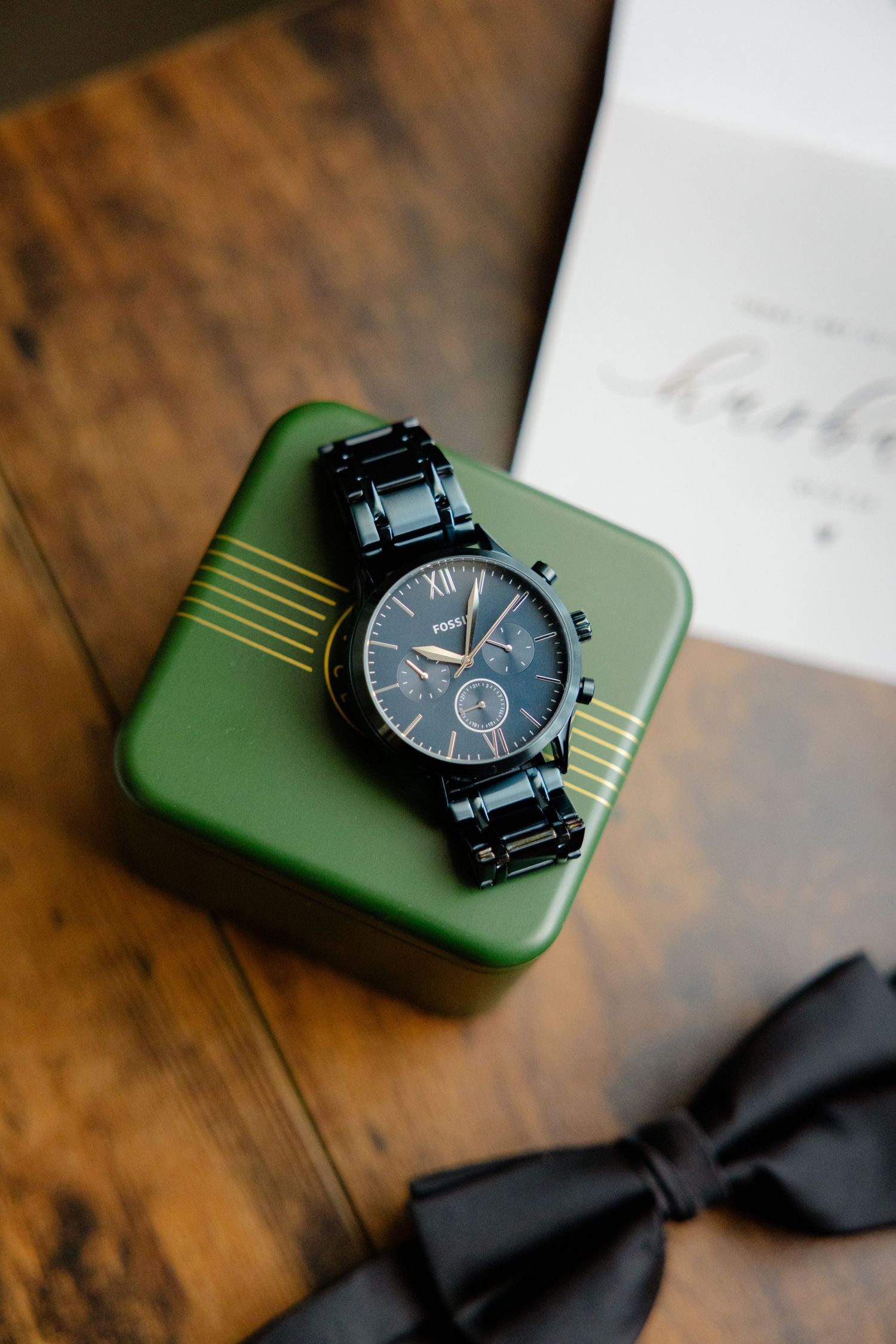 Black chronograph watch on green surface with black bowtie in background.