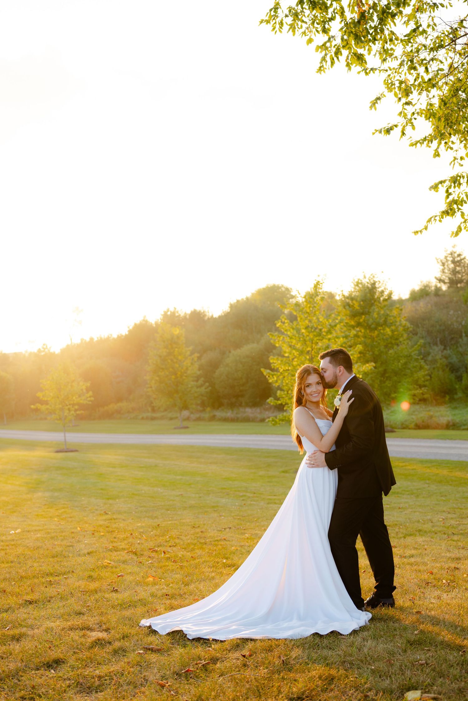 Newlyweds share an intimate moment during sunset in a scenic outdoor setting with glowing golden light.
