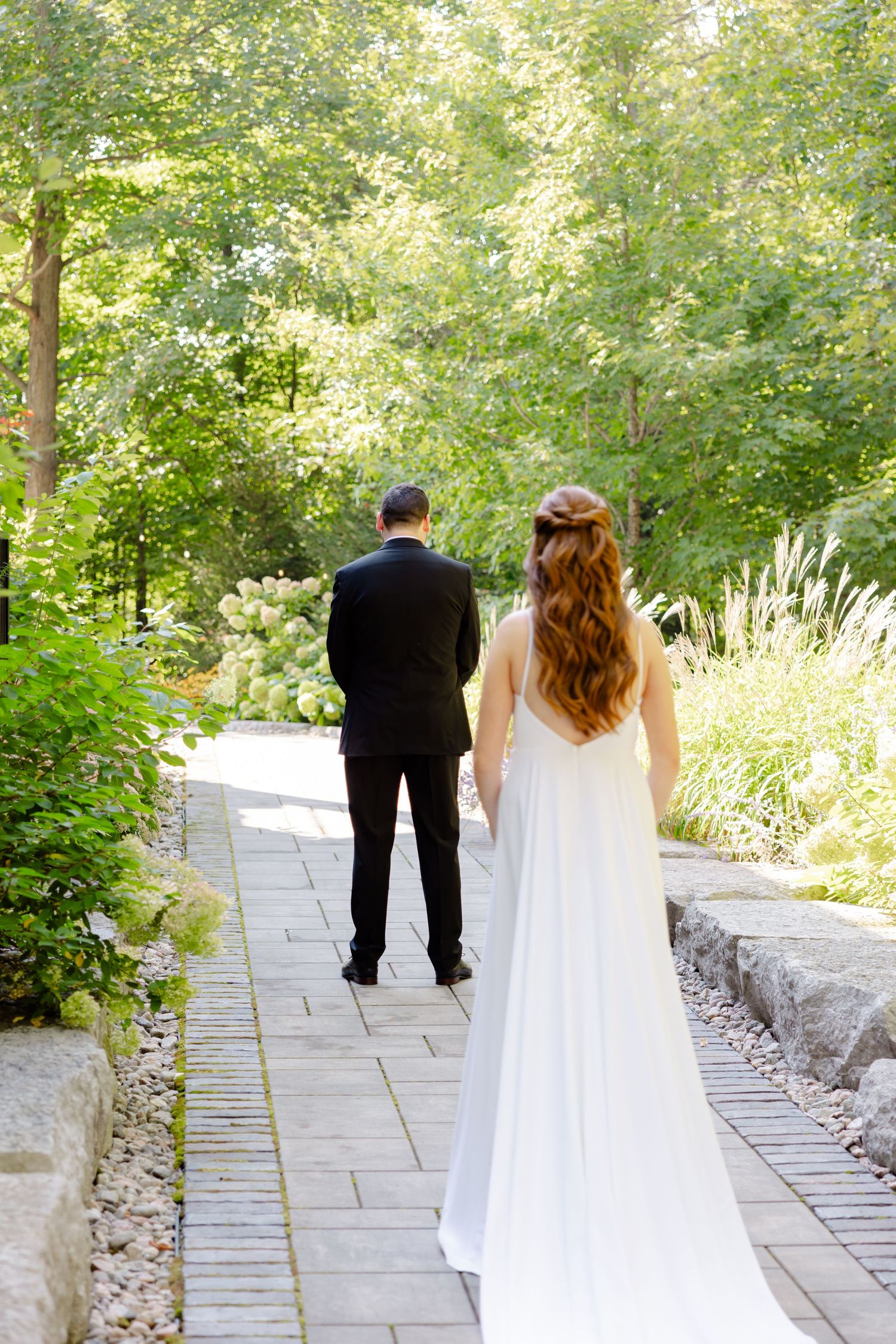 Couple shares first look moment on garden path with lush greenery surrounding them.