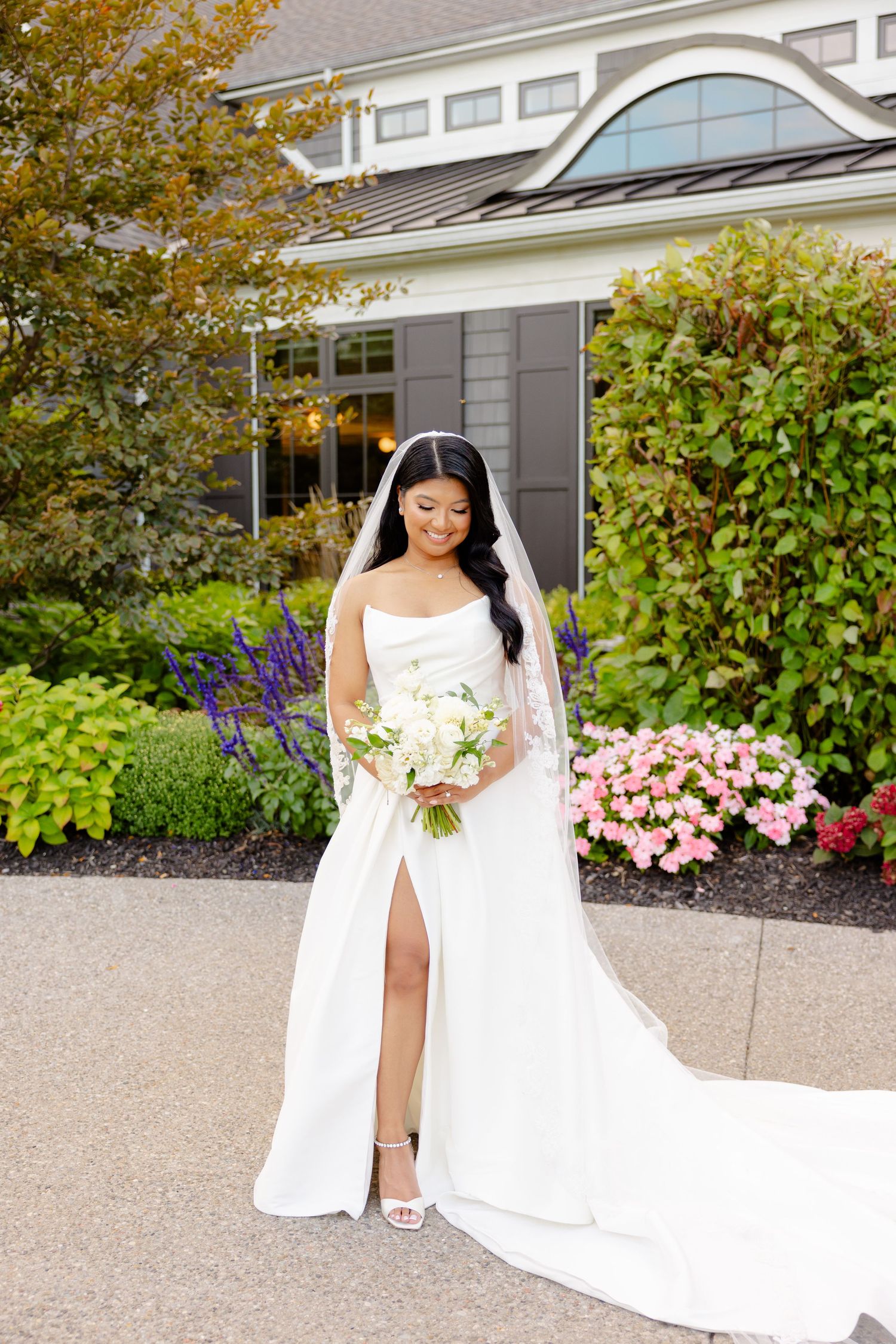 Elegant bridal portrait showcasing white gown and bouquet against landscaped garden background.