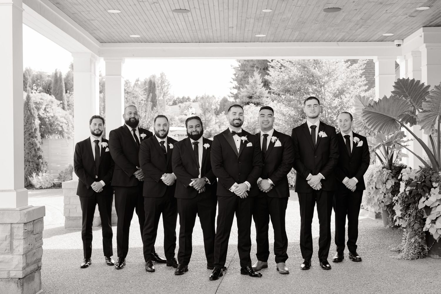 Black and white photo of wedding party in tuxedos lined up under a covered porch.