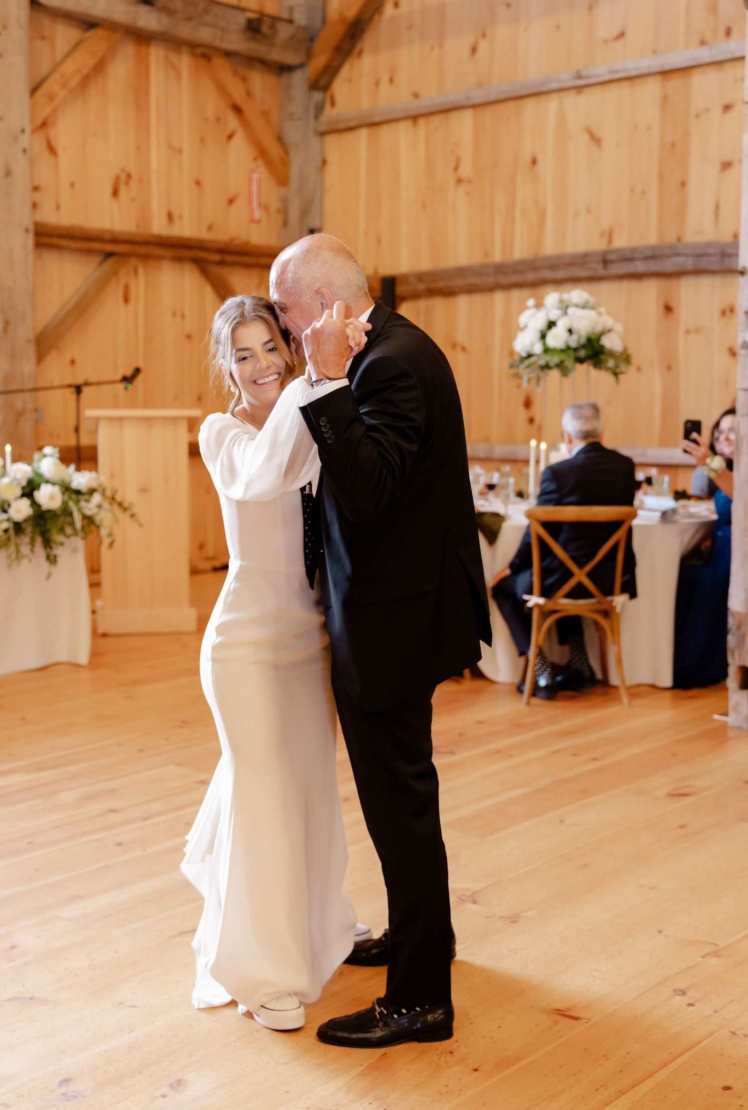 A couple shares their first dance in a rustic barn venue with wooden walls and floors.