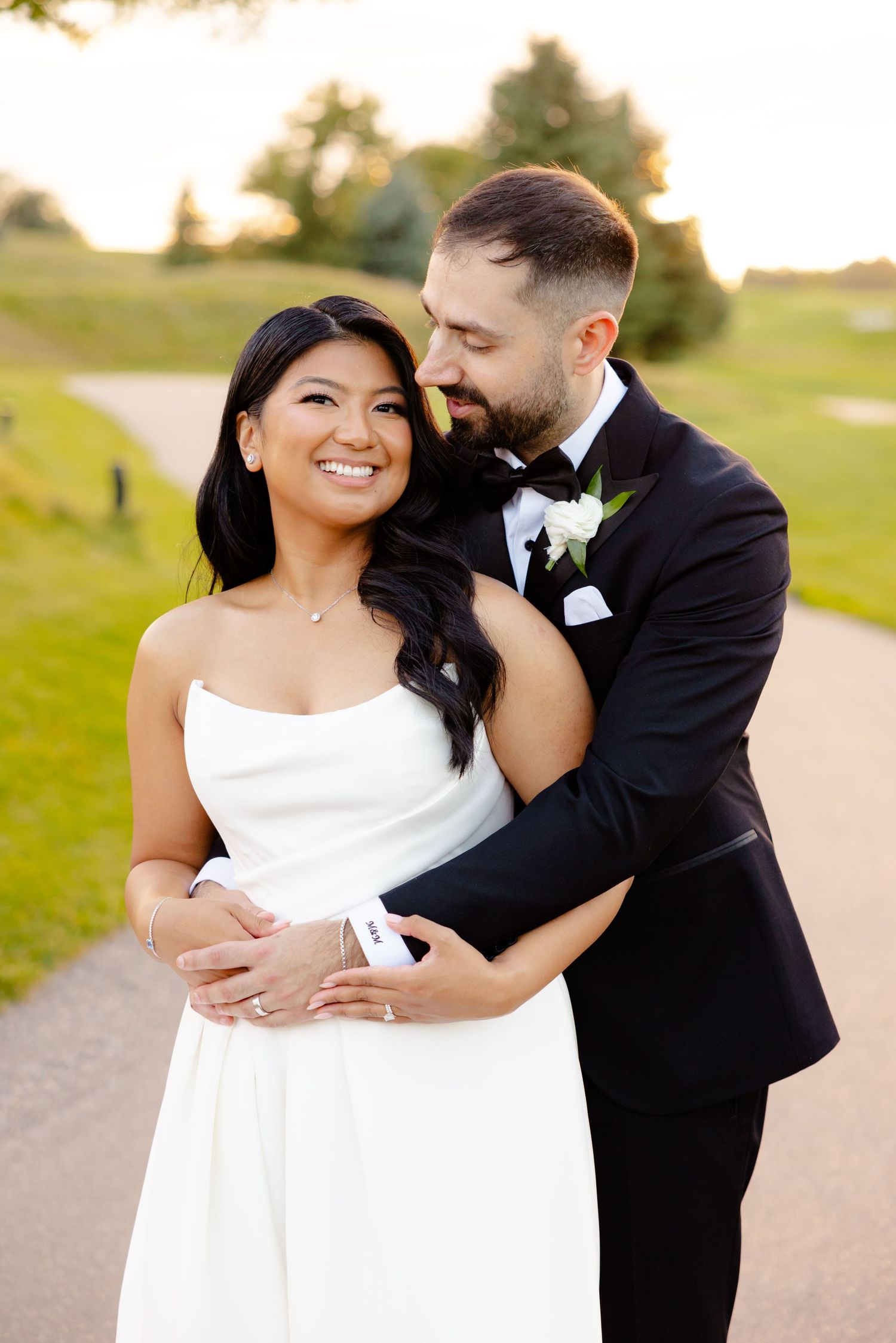 Joyful couple embraces on path with scenic golf course background at sunset.